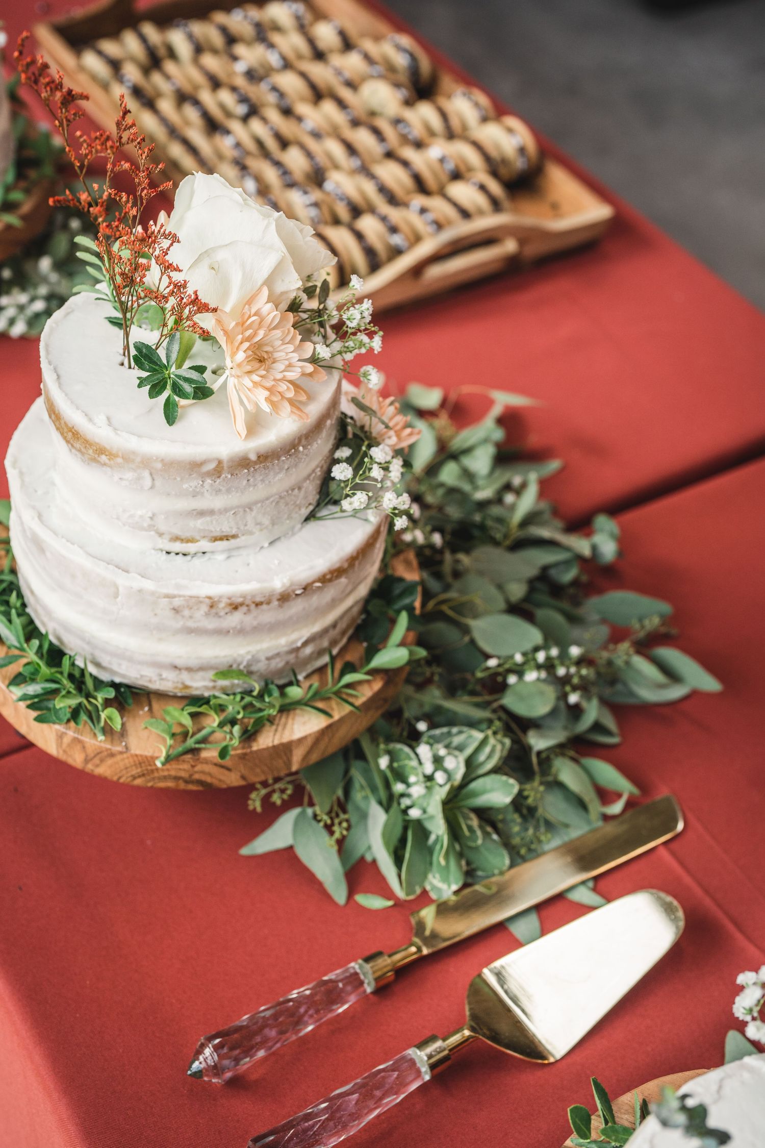 Small wedding cake adorned with fresh eucalyptus leaves and delicate flowers on a rustic wooden base.