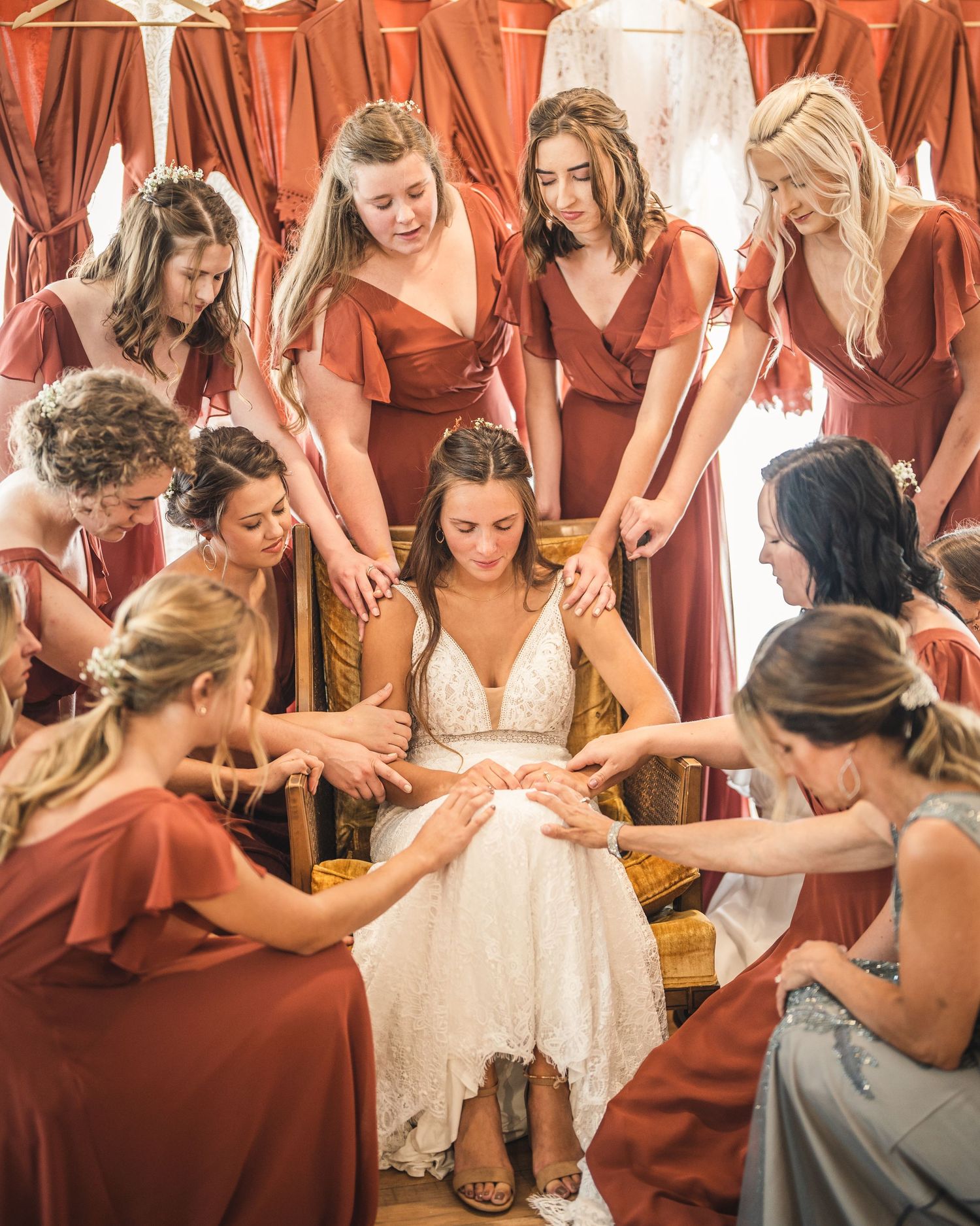 Bridesmaids in rust-colored dresses surround someone in a white wedding gown.