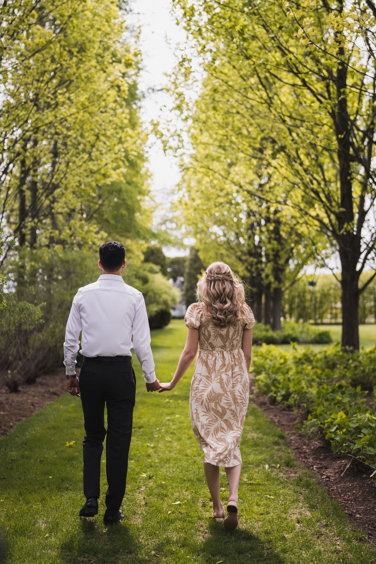 Couple walking through tree-lined path in lush garden setting.