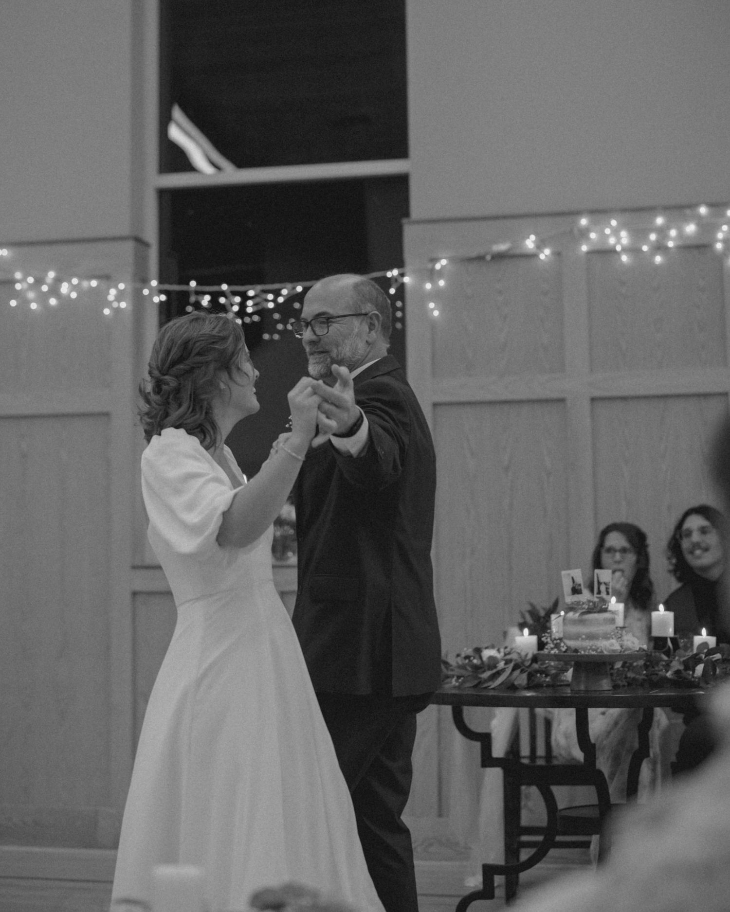 Couple dancing in a church hall decorated with twinkling lights for their wedding reception.