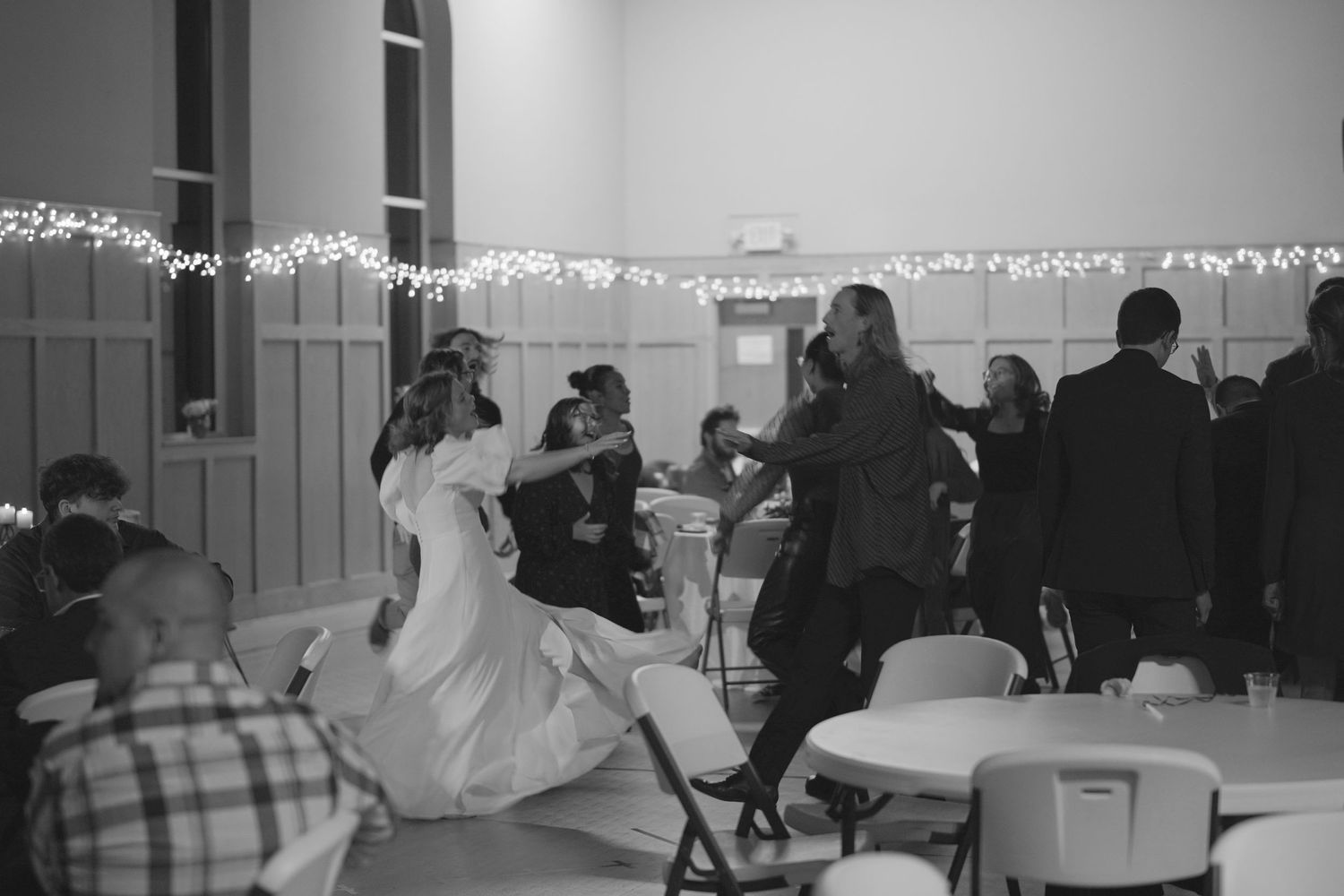 An indoor event space decorated with string lights and tables for a celebration.