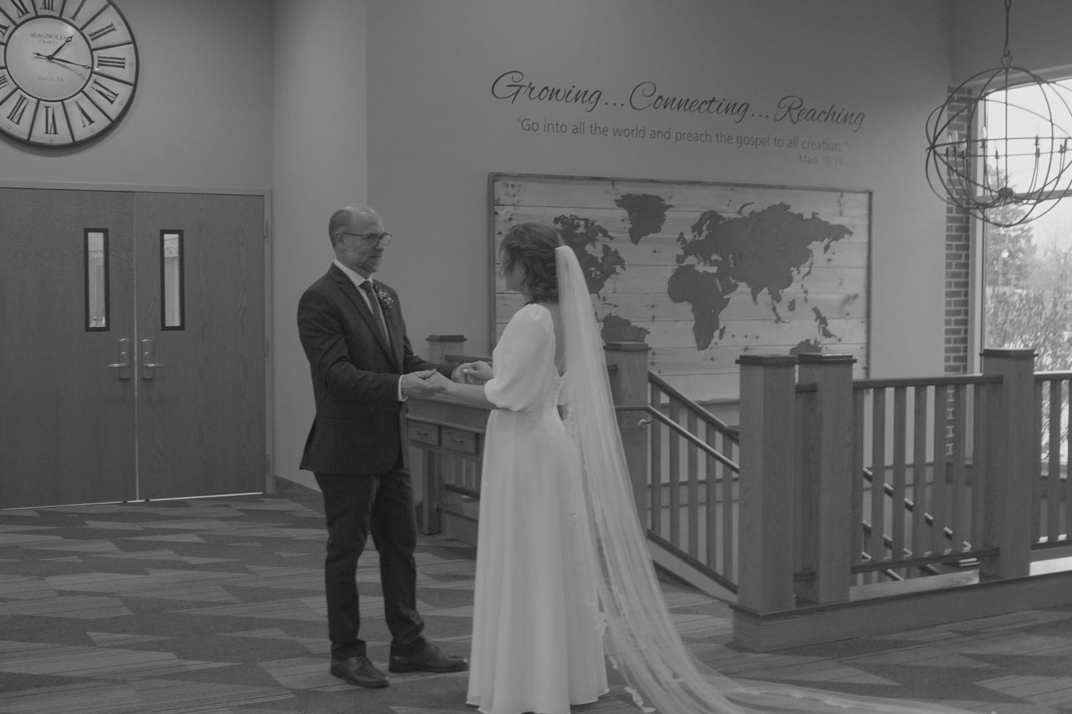 Wedding couple shares intimate moment in church hallway with decorative world map backdrop.
