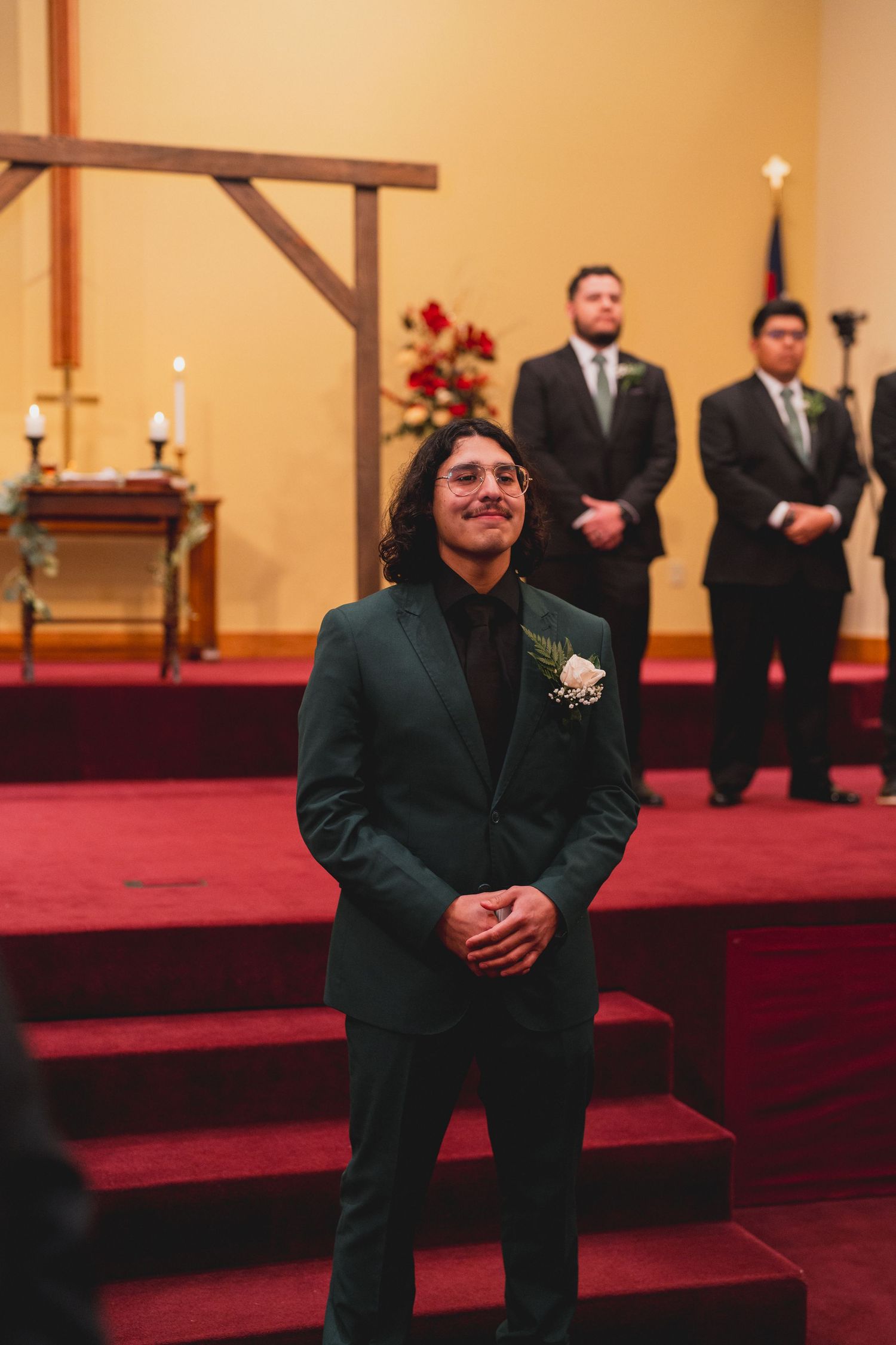 Wedding party members seated on red carpeted church steps during ceremony.