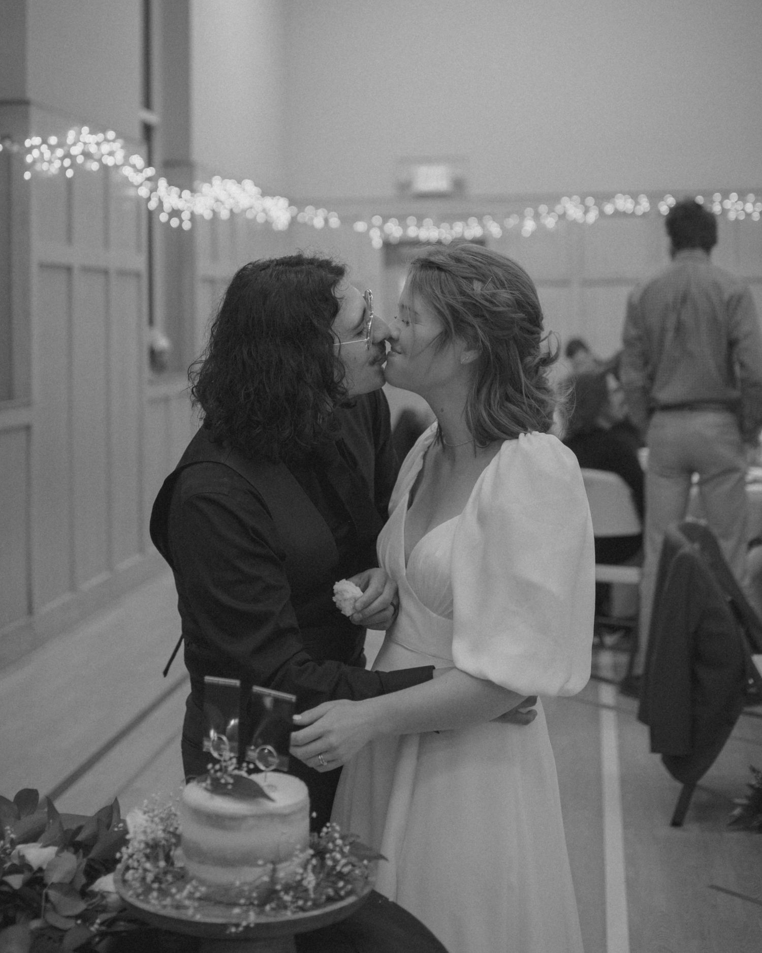 A couple shares an intimate dance moment in black and white at an indoor venue with string lights.