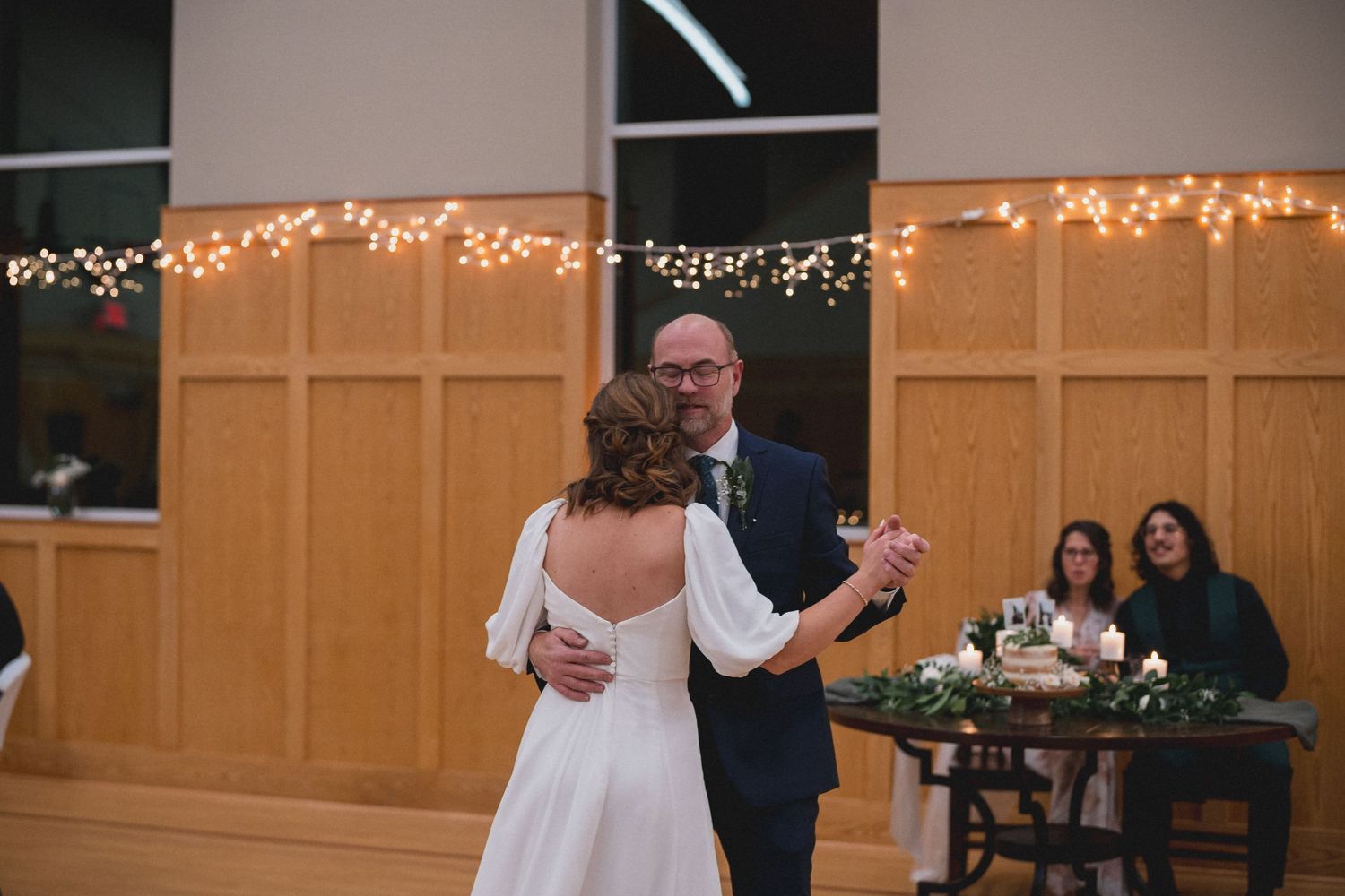 Wedding celebration in a church hall with string lights and wooden decor.
