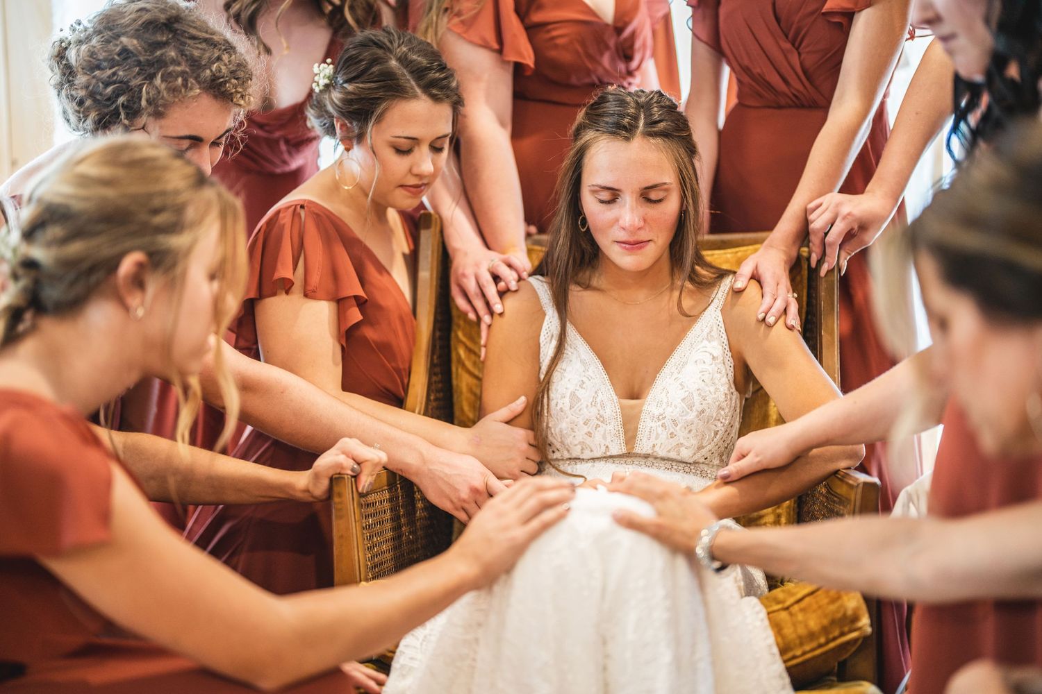 Emotional wedding moment with bridesmaids in rust dresses surrounding bride in white gown.