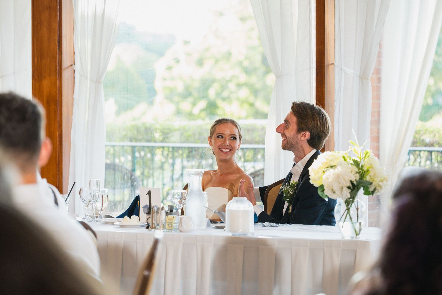 A smiling bride and groom share a joyful moment together at their elegant wedding reception head table.