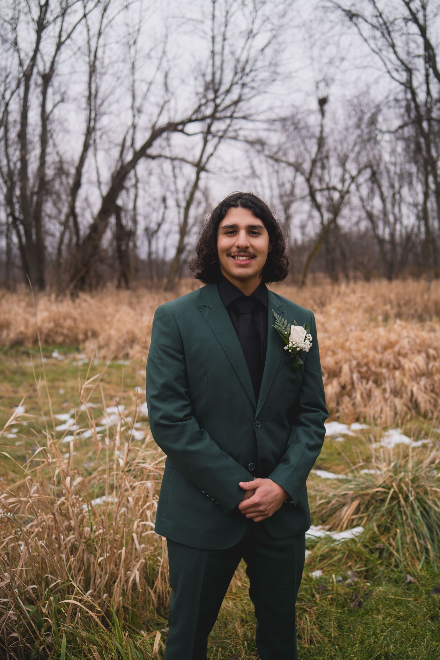 Wedding portrait of person in emerald green suit with boutonniere against autumn grasses.
