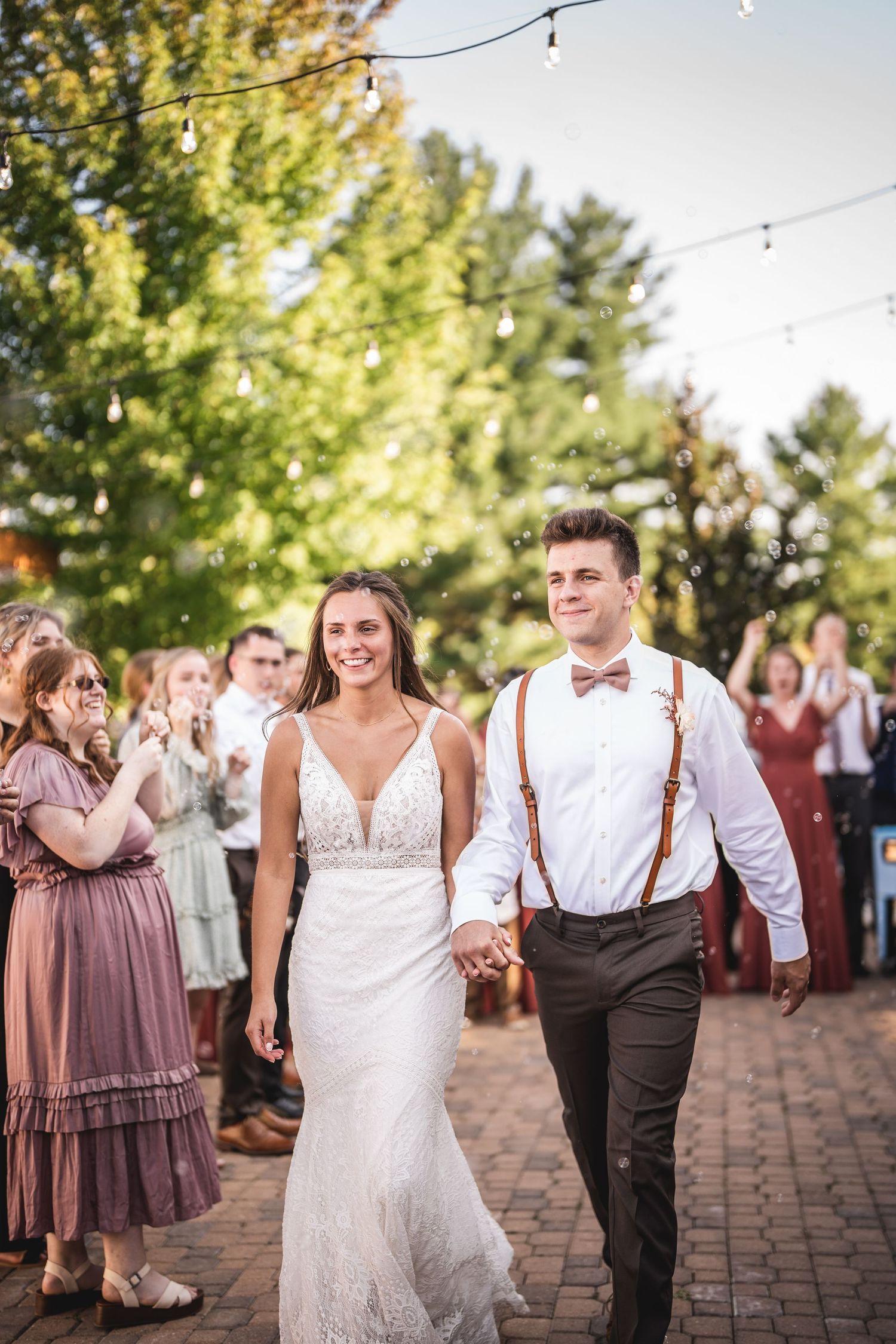Wedding party walking along brick pathway during outdoor celebration with string lights.