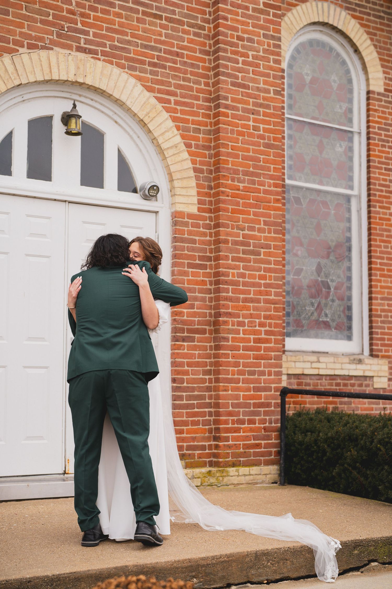 Wedding photographer captures candid moments of a couple by a brick church entrance.