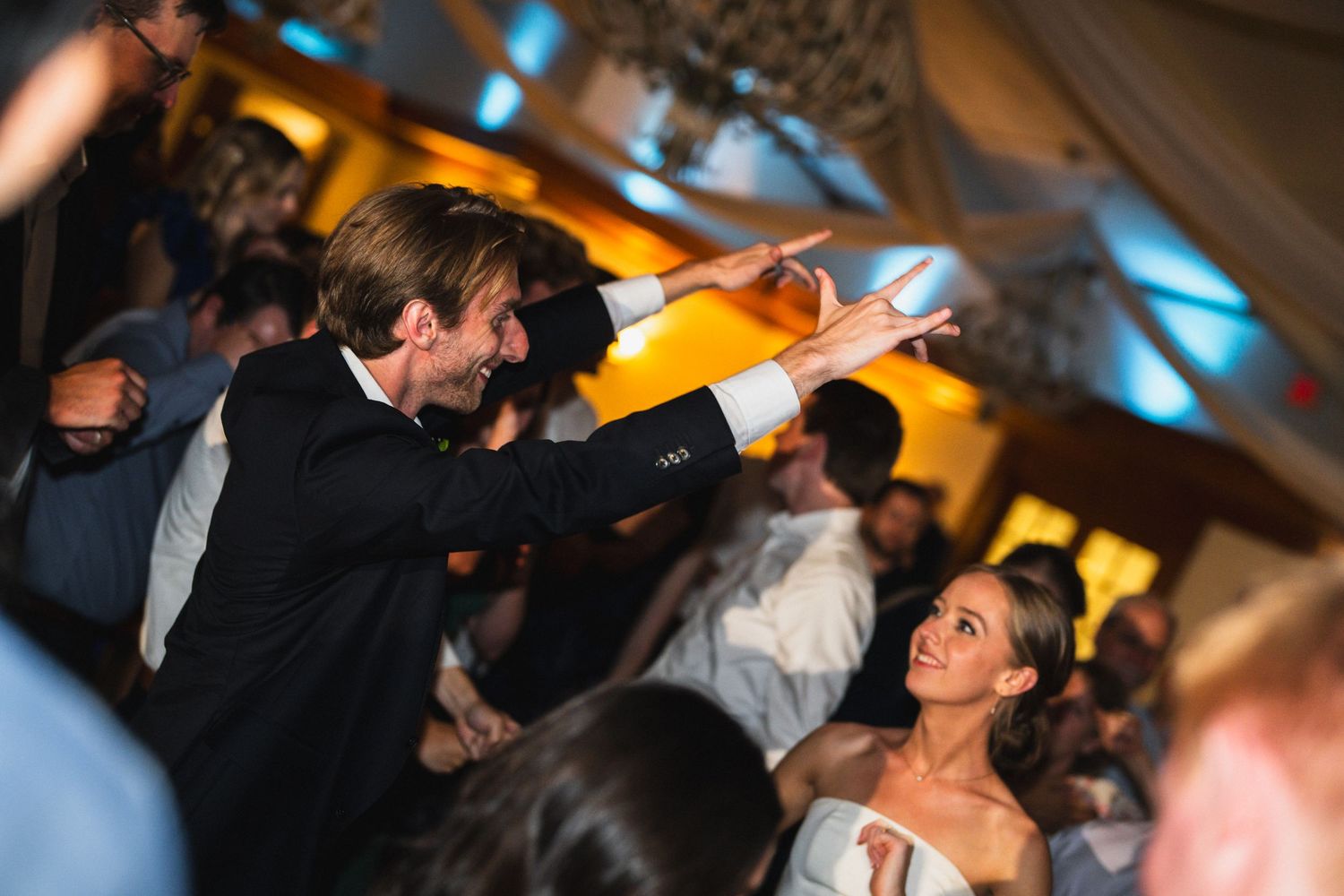 Bride and groom dancing joyfully with guests at elegant indoor wedding reception celebration.