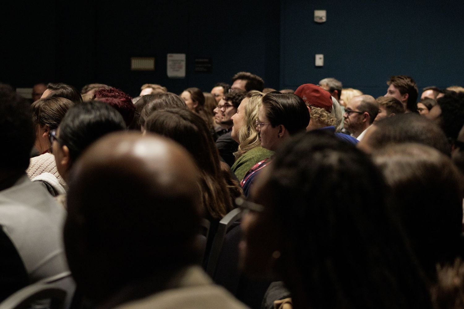 Crowded audience sitting in a dark theater or auditorium.
