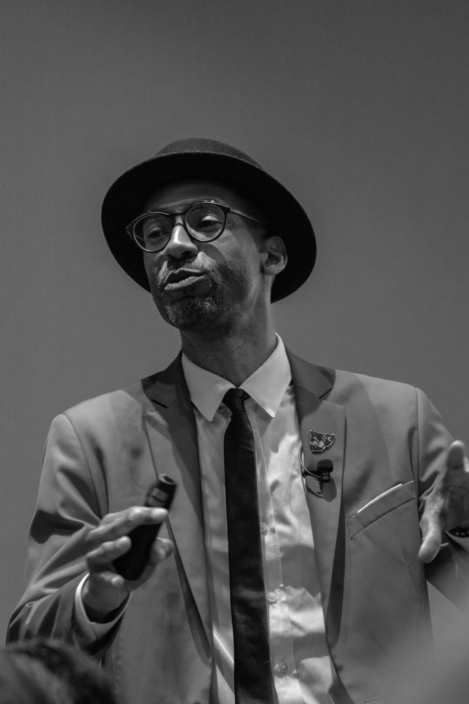 Stylish portrait of someone in suit and hat against gray background.