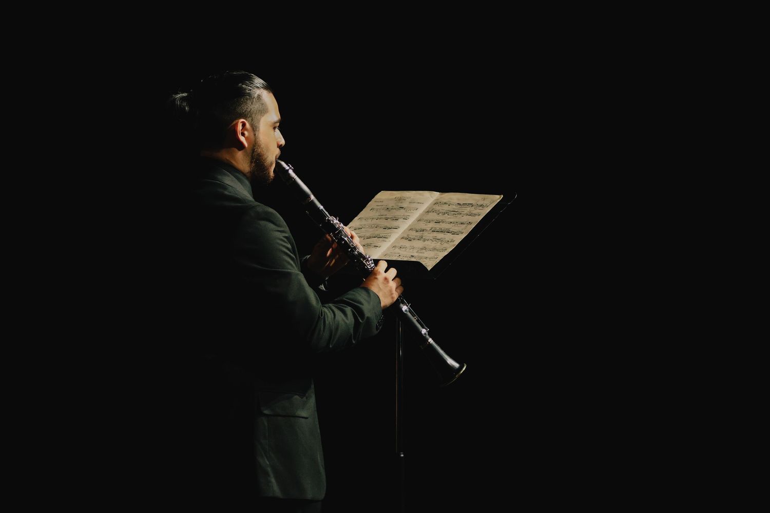 A silhouetted performer singing on a dark stage with dramatic lighting.
