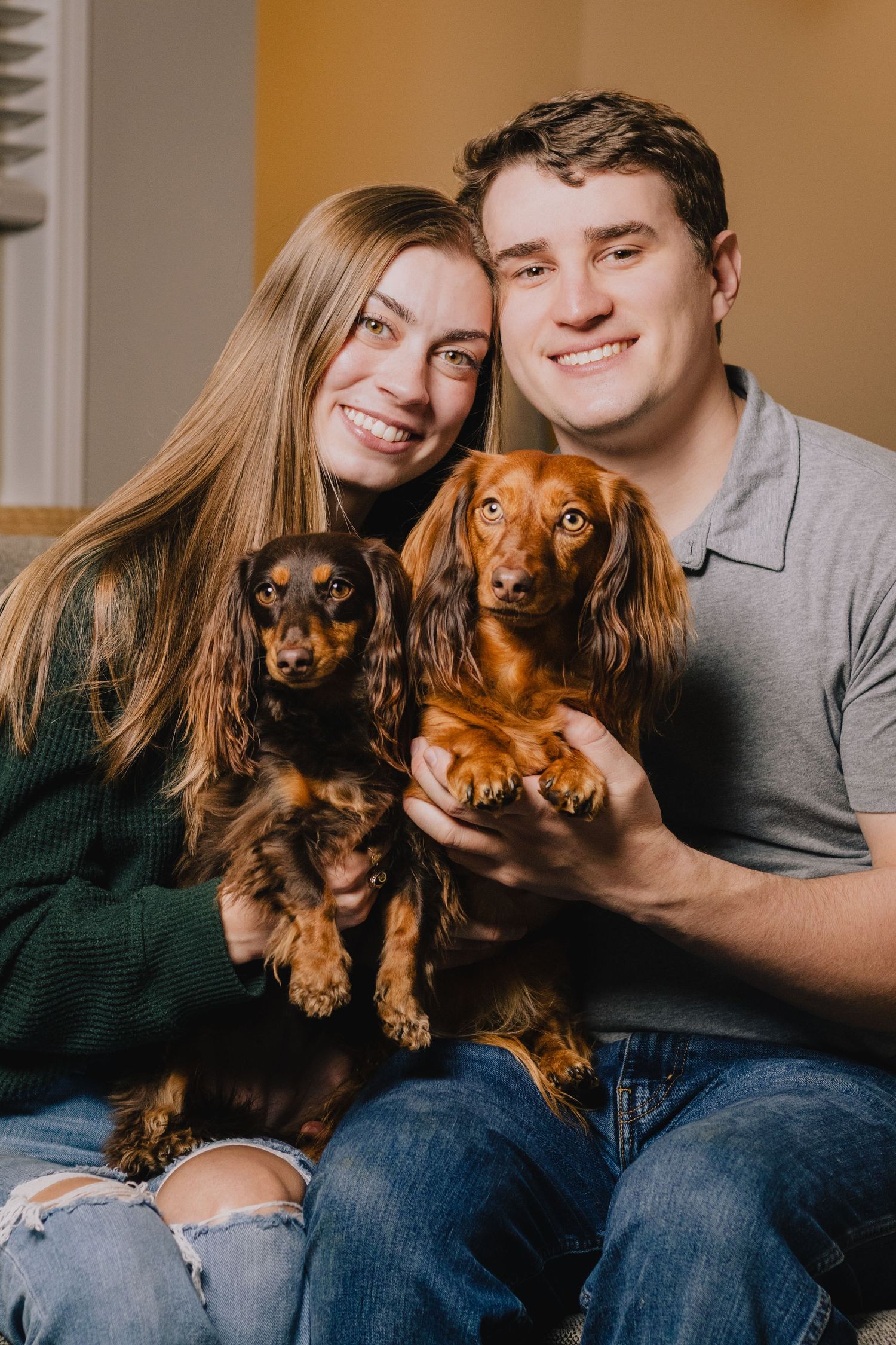 A couple poses with their adorable long-haired dachshund dog in a series of candid indoor photos.