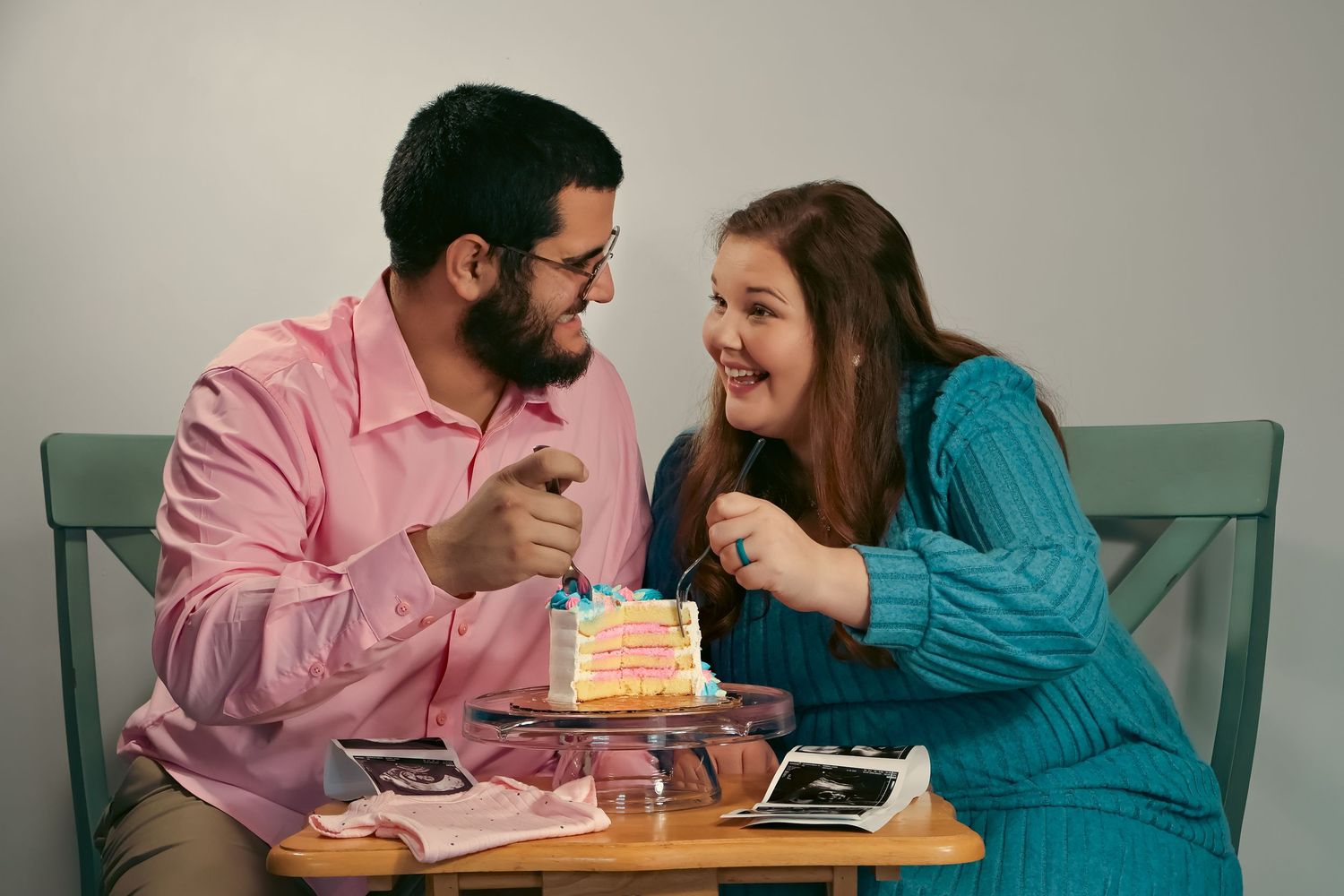 Couple sharing a pink gender reveal cake while sitting on blue chairs.