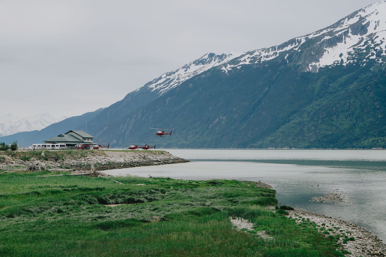 Panoramic view of snow-capped mountains and coastline under cloudy skies.