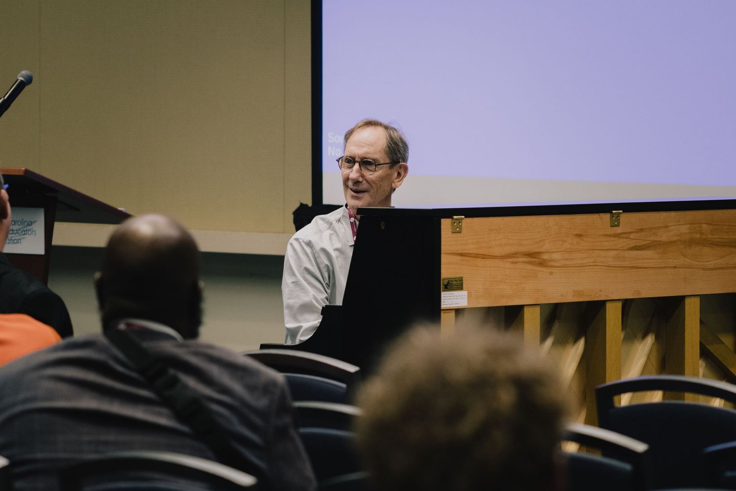 Speaker presenting at a piano during an educational seminar.