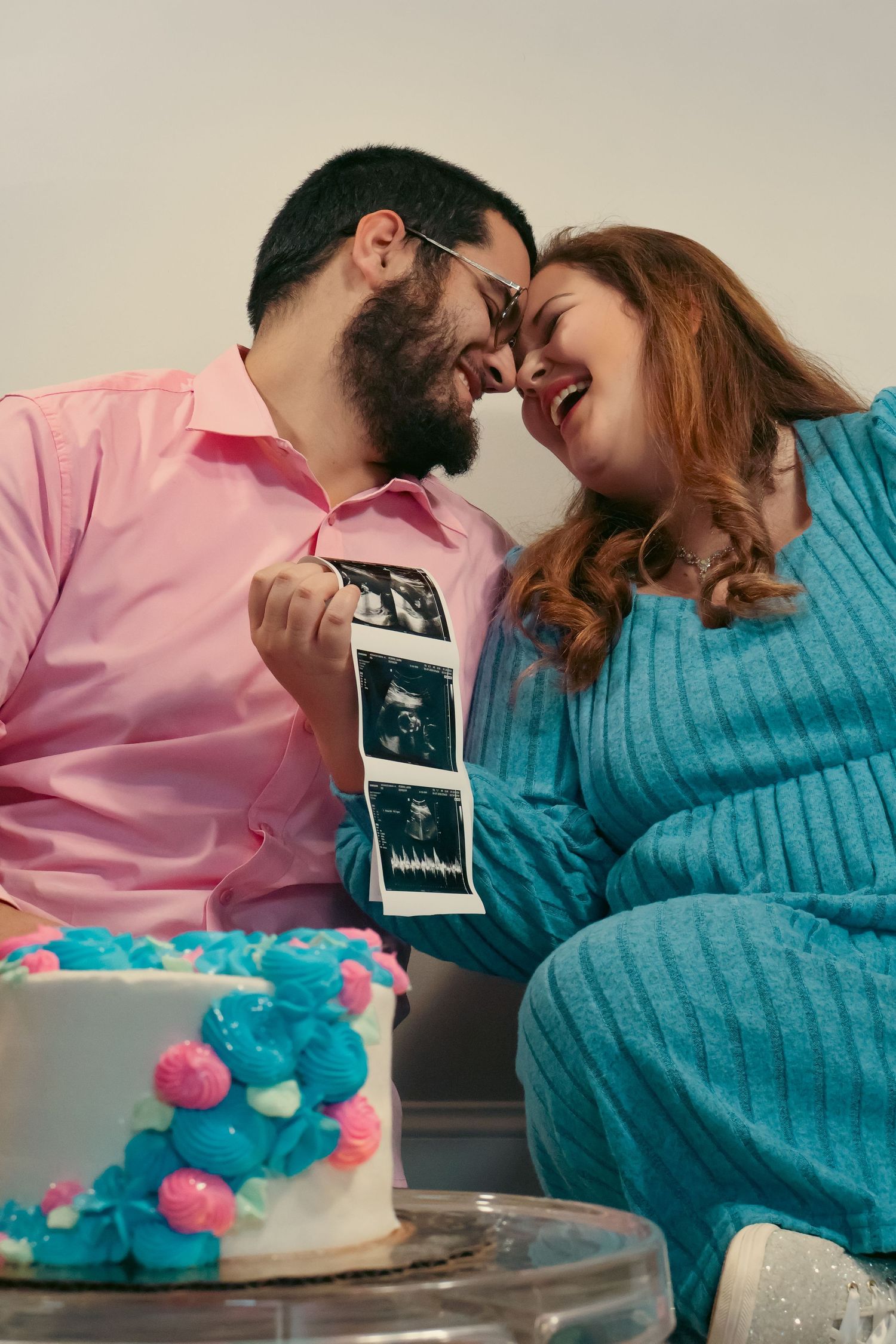 Couple shares intimate moment with cake and ultrasound photos in celebration setting.