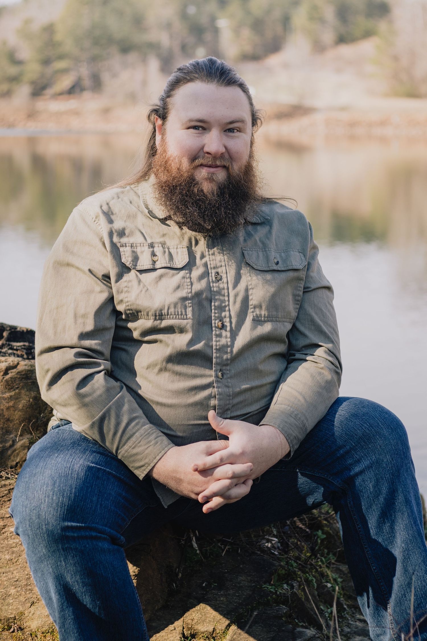 Outdoor portrait of someone in casual attire sitting by a lake.