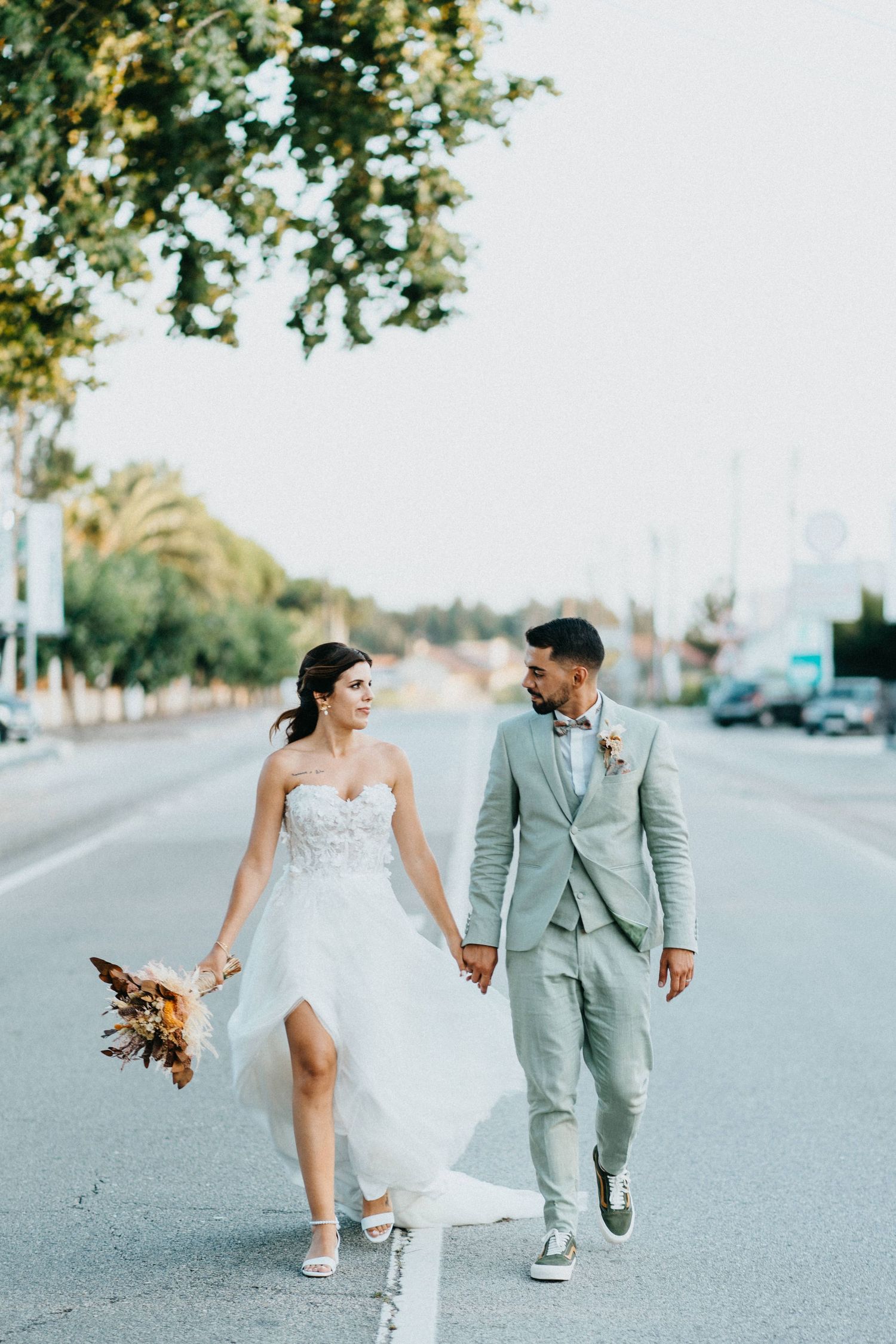 Couple in wedding attire playfully walking down an urban street.