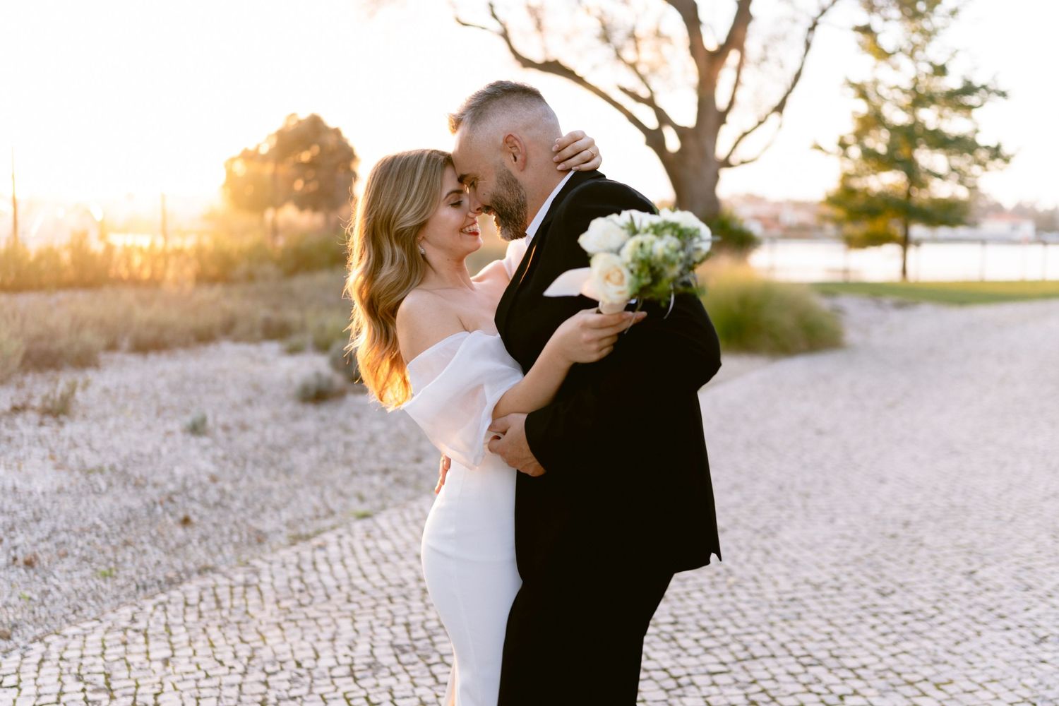 Couple shares intimate wedding moments at sunset on cobblestone pavement.