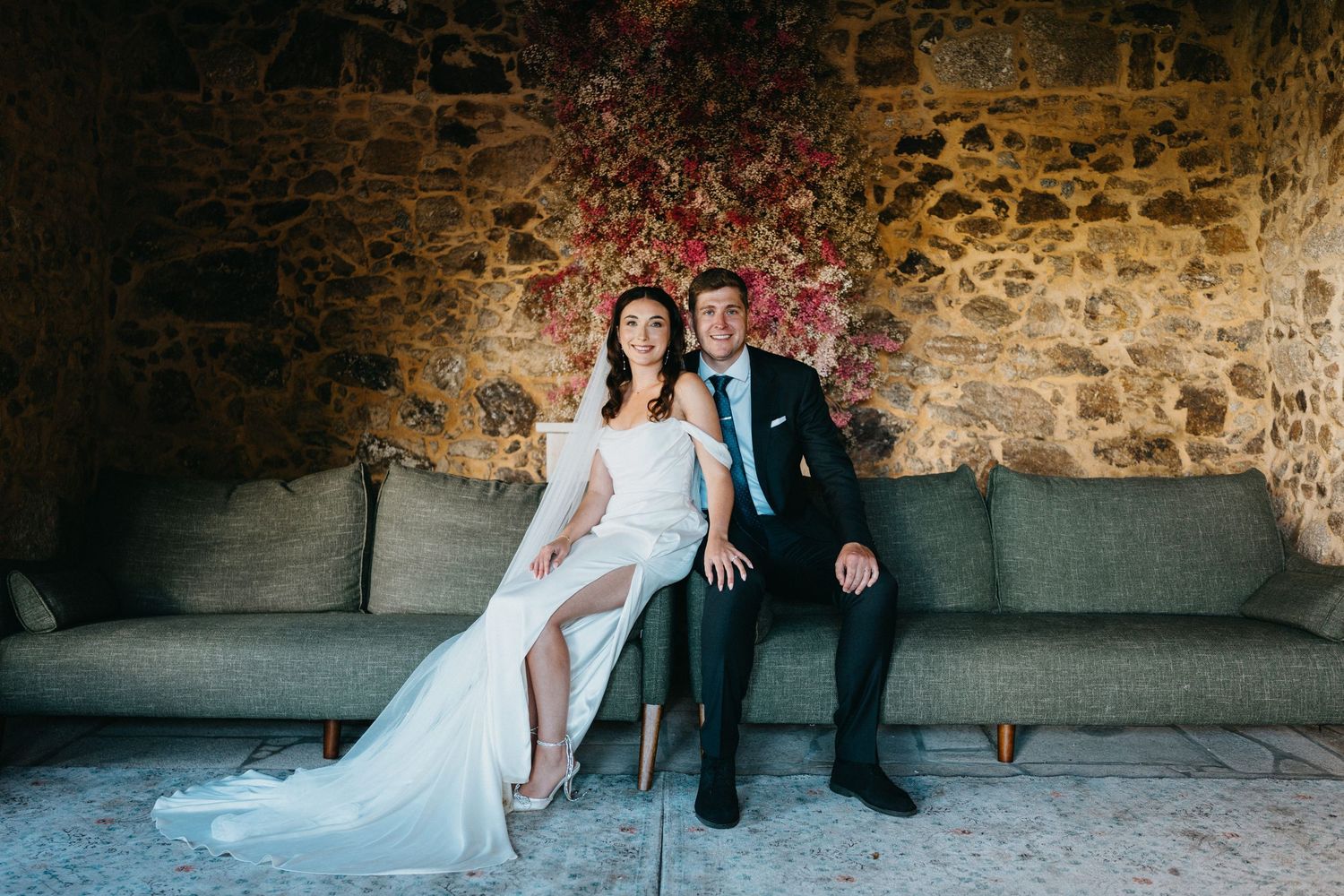 Wedding couple poses against rustic stone wall in romantic portrait series.