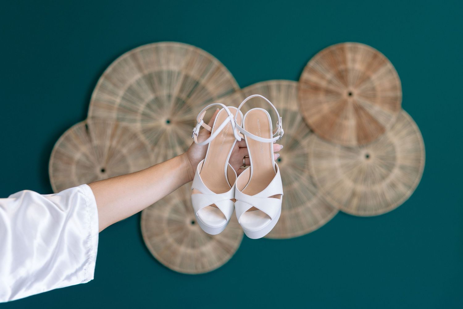 White bridal shoes displayed against a teal background with decorative circular elements.