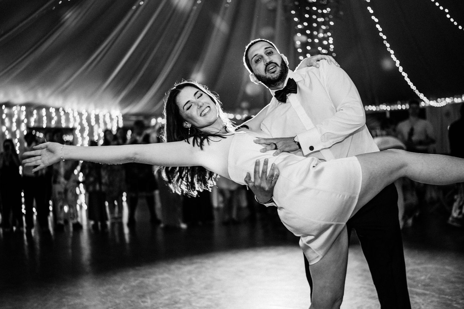 A couple shares a playful dip dance moment under twinkling lights at their wedding reception.