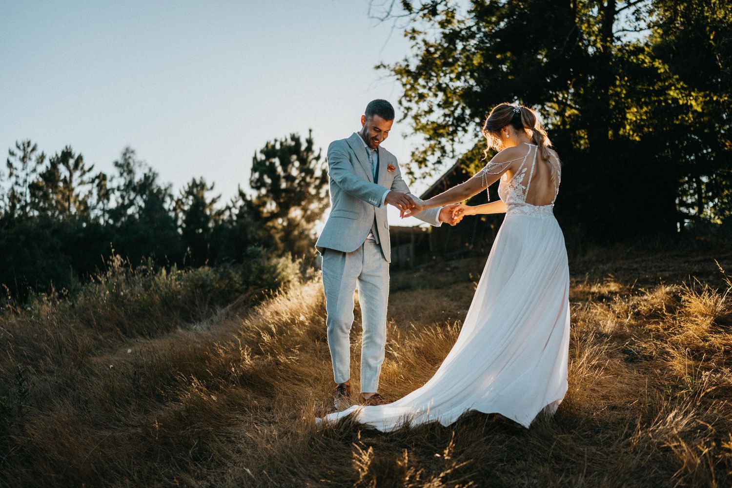 Wedding couple walking through sunlit field during golden hour.