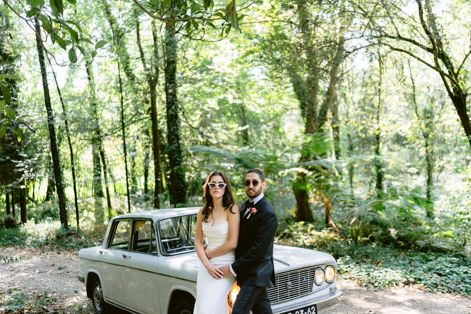 Wedding couple poses in wooded park setting with vintage car.