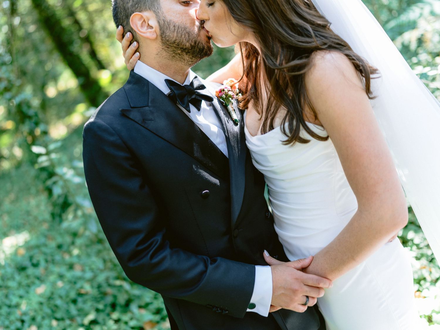 Tender moment between newlyweds surrounded by green foliage and natural light.