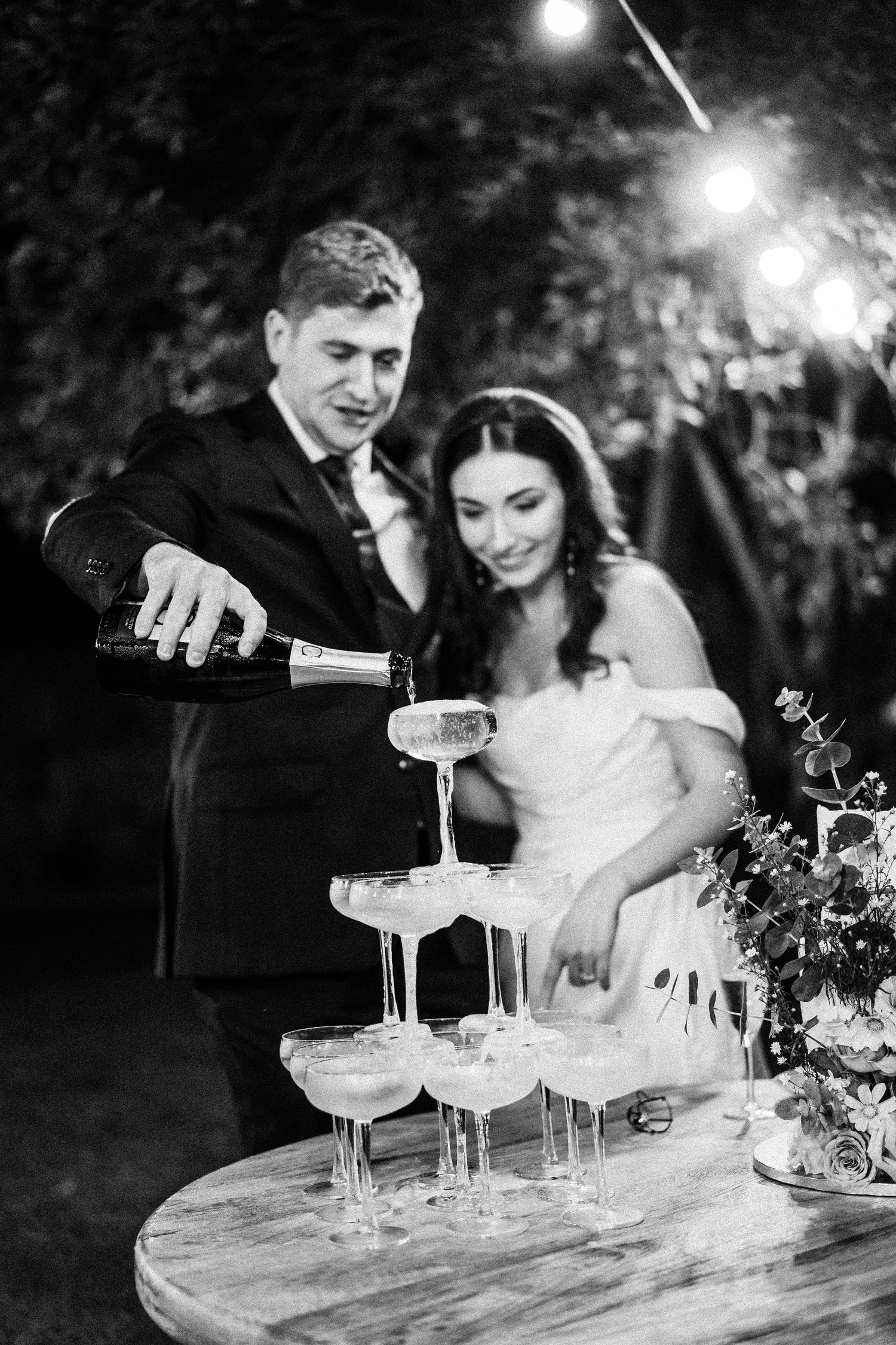 Champagne tower being poured at nighttime wedding celebration.