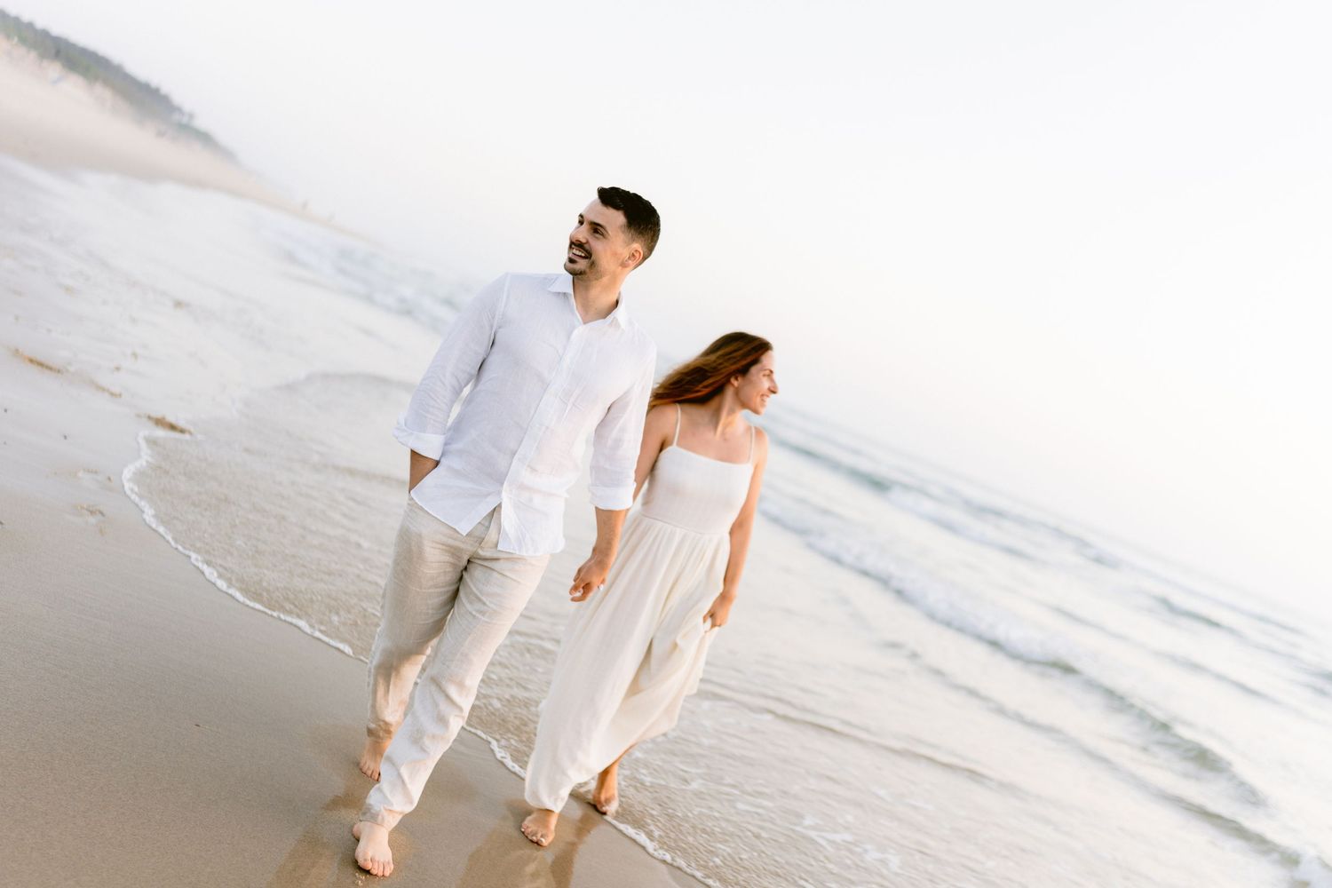 Couple walking hand in hand along a serene white sandy beach.