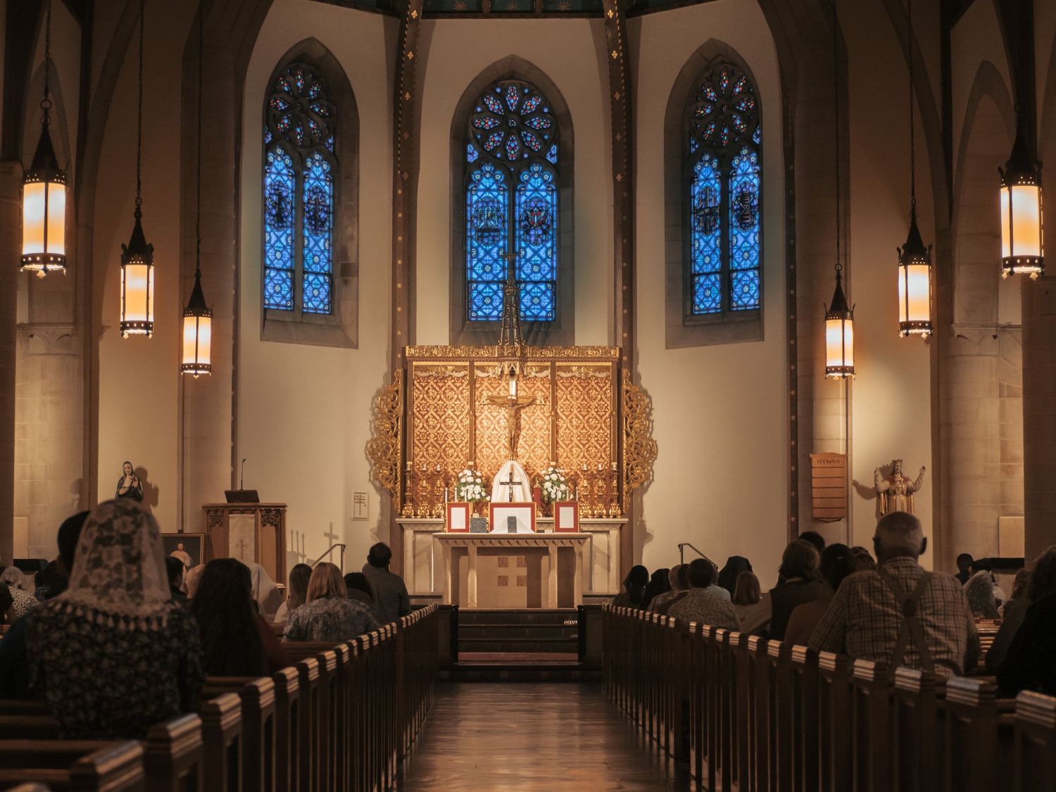 Congregation gathered inside Saint Rita Catholic Church in Alexandria, Virginia with gothic arched stained glass windows and ornate altar.