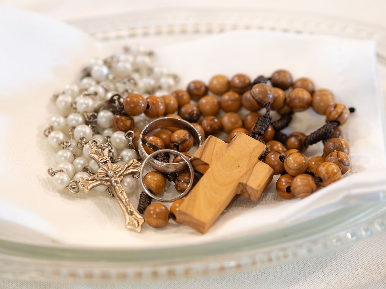 Wedding rings resting on white fabric with wooden rosary beads and crucifix for ceremony.