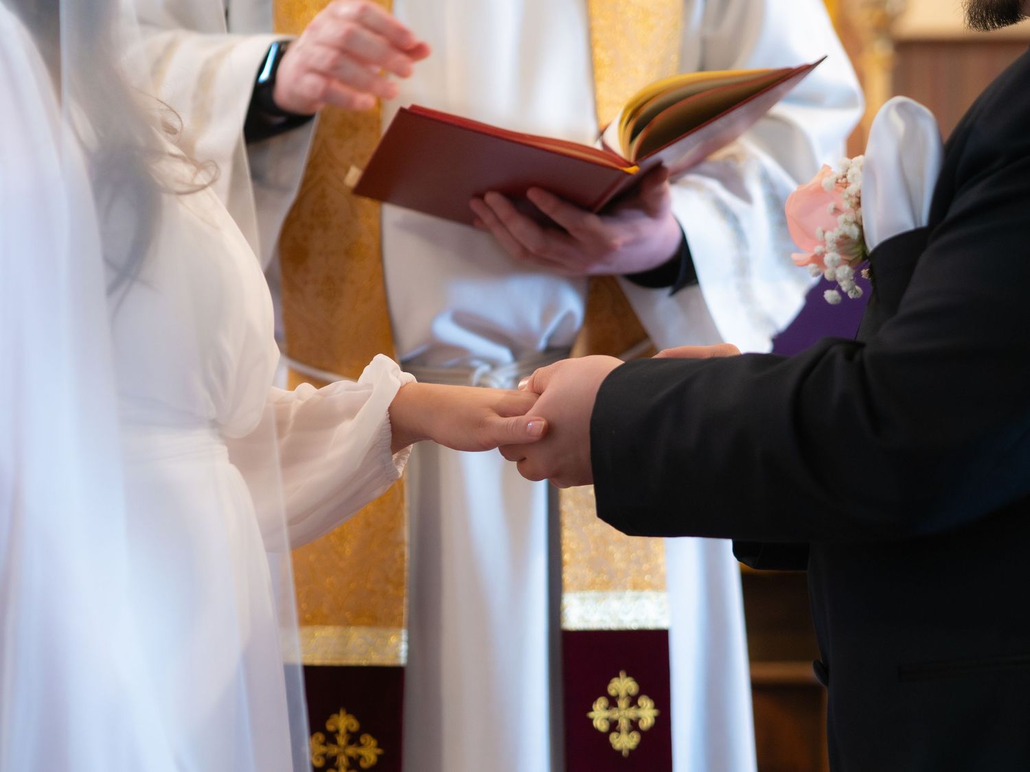 A priest holds a book as a bride and groom exchange rings during a traditional church wedding ceremony.