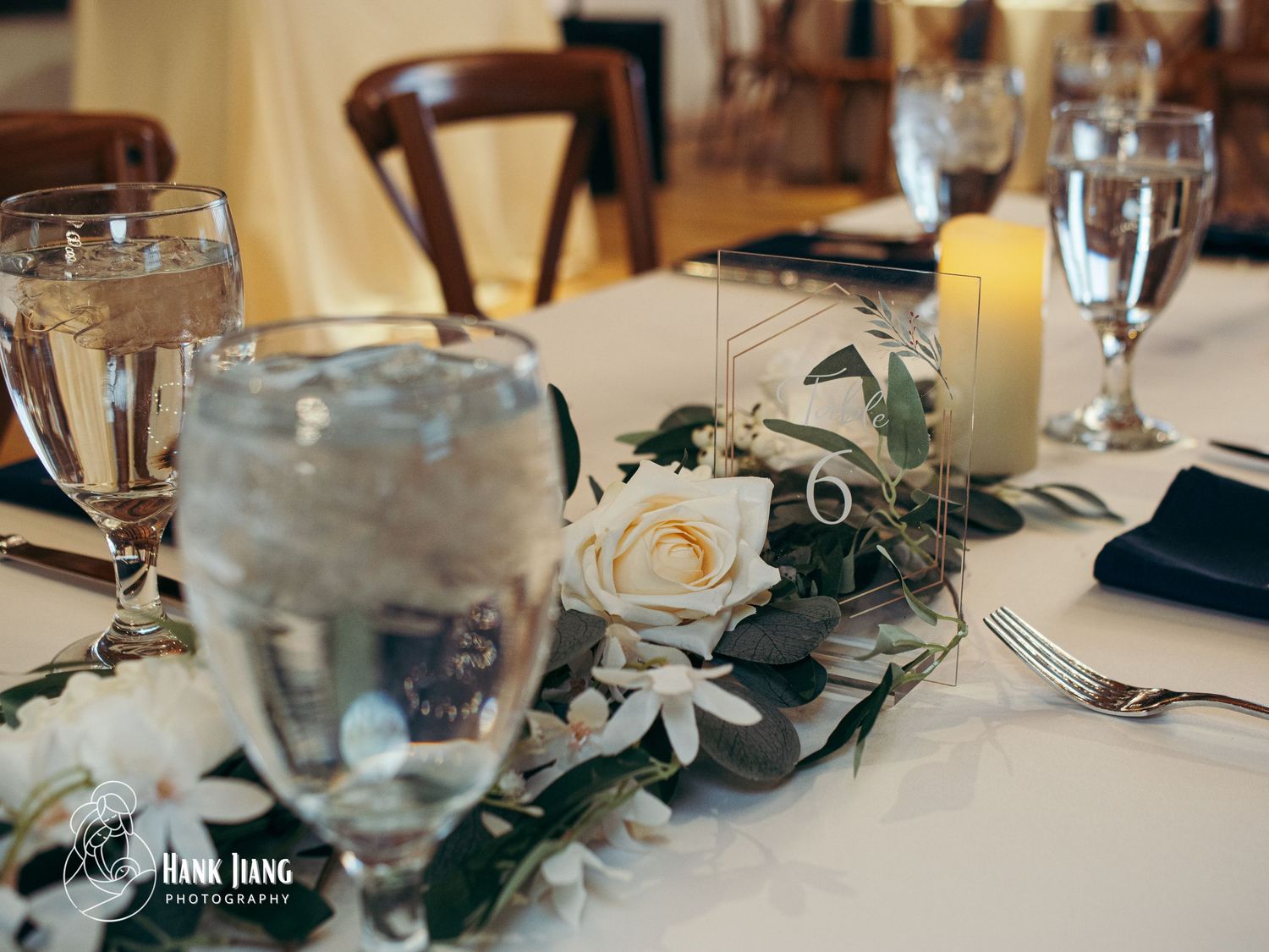 Elegant wedding table centerpiece with white roses, greenery garland, candles, and navy napkins at a reception venue.
