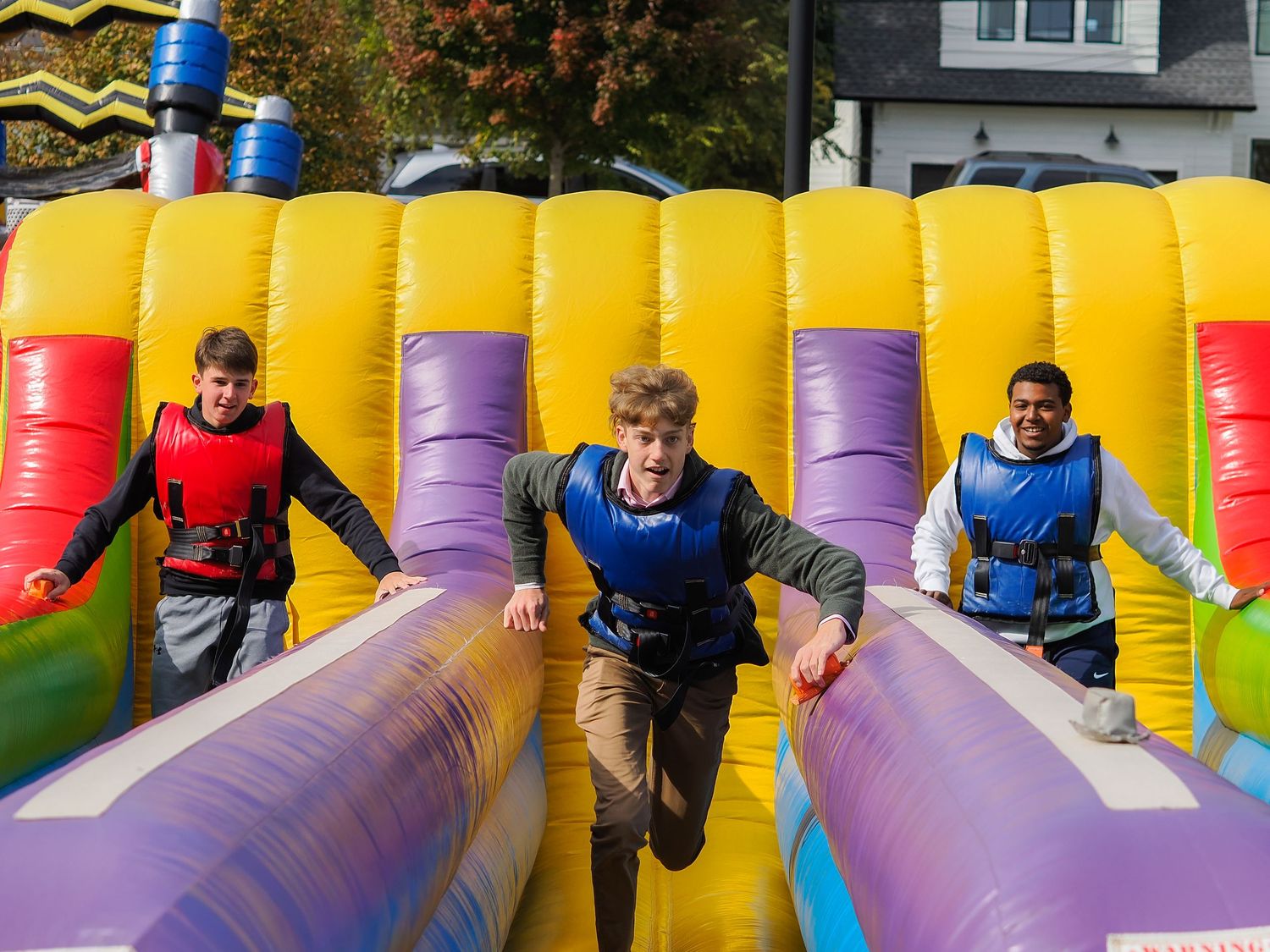 Three teens racing through colorful inflatable obstacle course at outdoor carnival event.