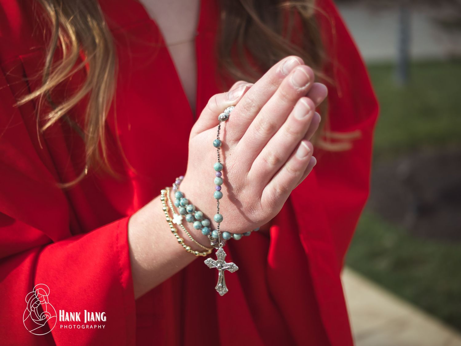 Woman in red dress praying with turquoise rosary beads and cross bracelet, photographed by Hank Jiang Photography.