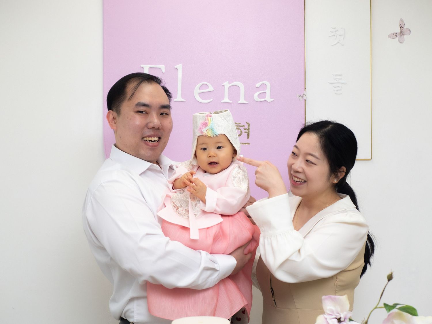 Happy Asian family celebrating baby's first birthday at Elena studio, parents smiling with infant.