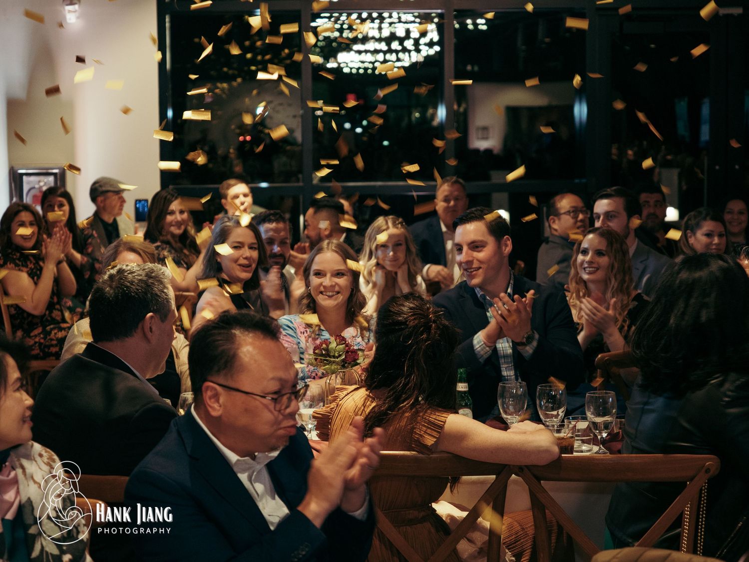 Joyful wedding reception crowd clapping with golden confetti falling in a festive restaurant celebration.