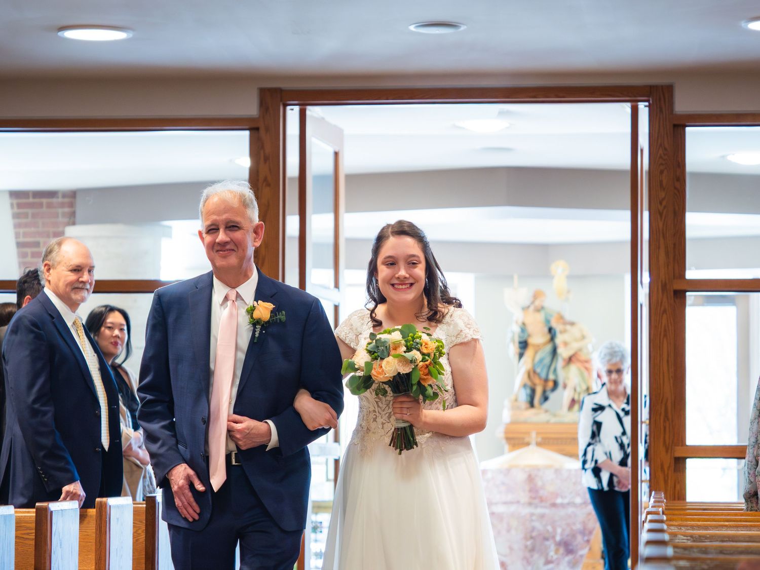 Bride walking down the aisle with her father in a Catholic church during a wedding ceremony.
