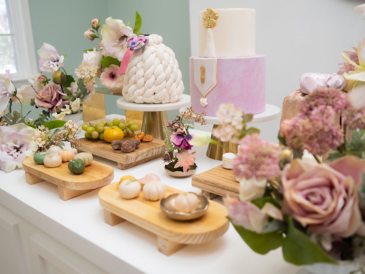 Elegant dessert table with floral arrangements, macarons, and tiered cakes for a Korean first birthday doljabi celebration.