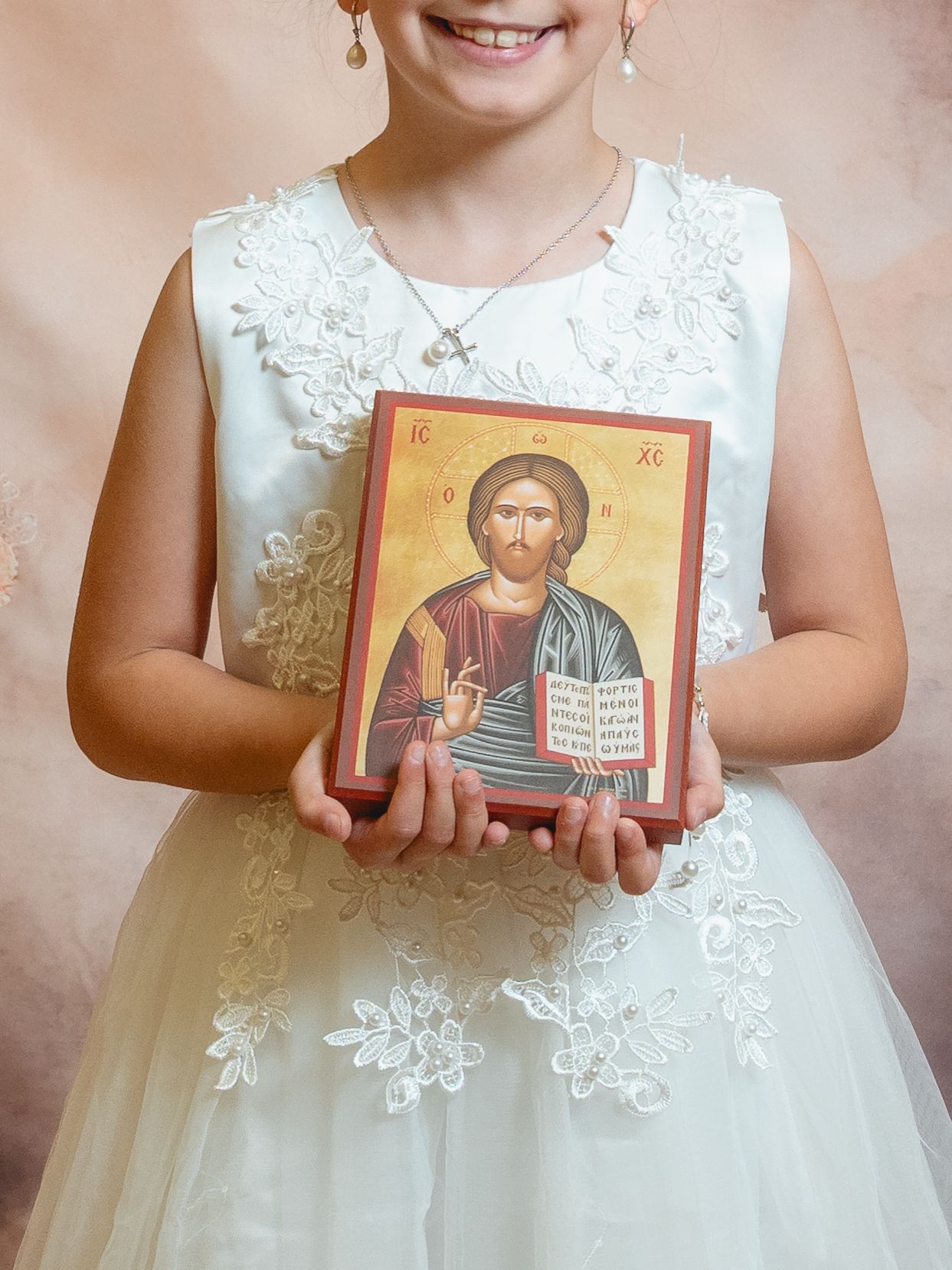 Young girl in white lace dress holding a Christian Orthodox icon of Jesus Christ during First Communion.