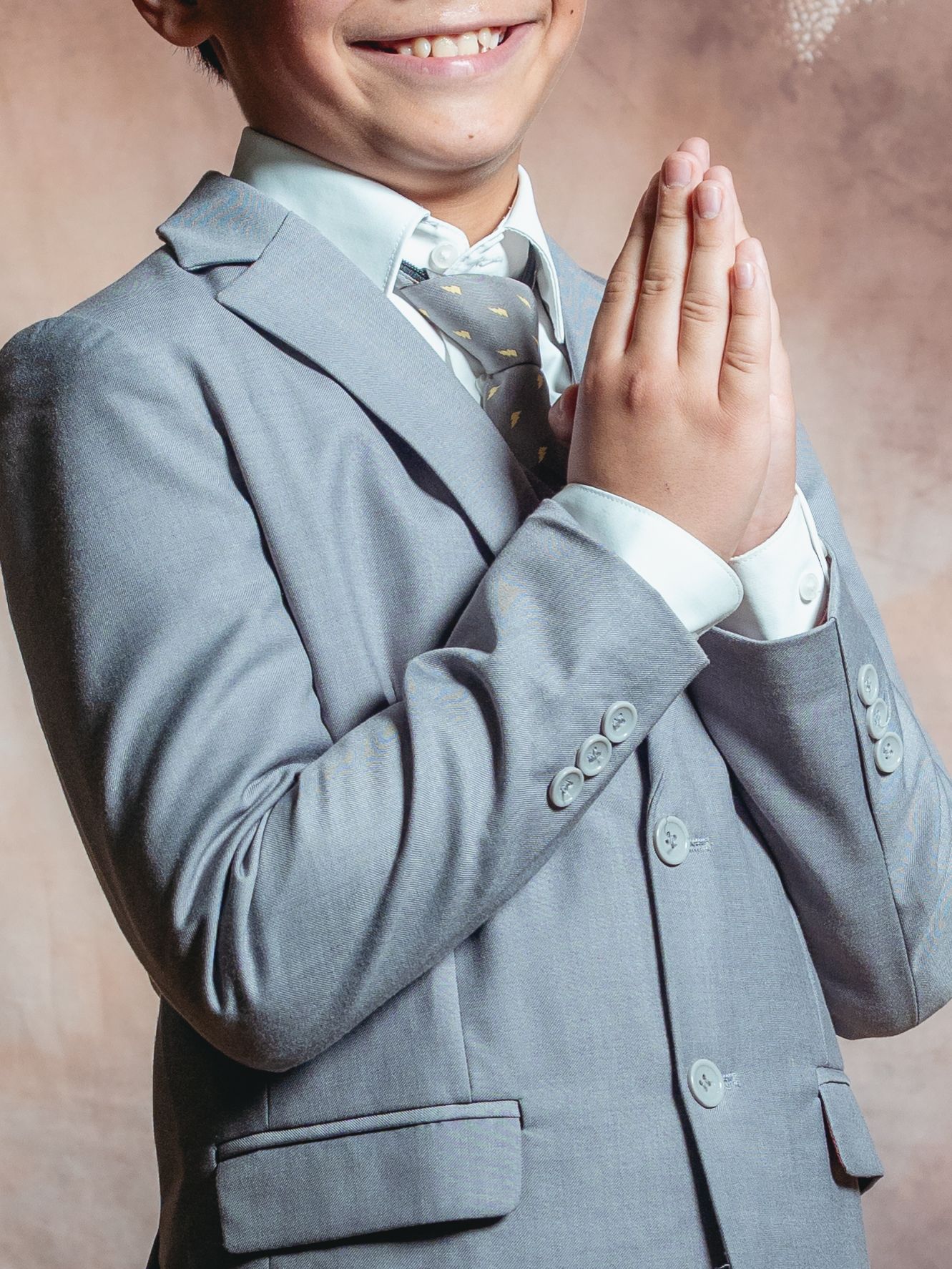Smiling boy in gray suit with hands pressed together in prayer pose for formal occasion.
