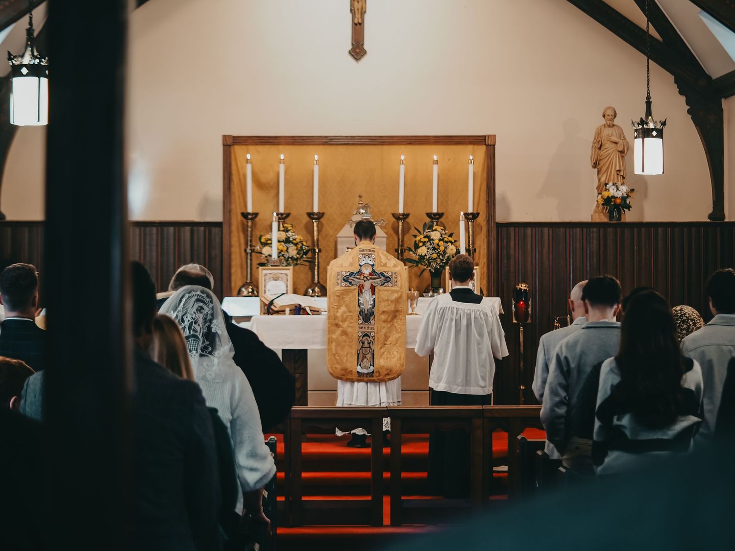 Congregation attending traditional Latin Mass with priest at ornate altar in small chapel.
