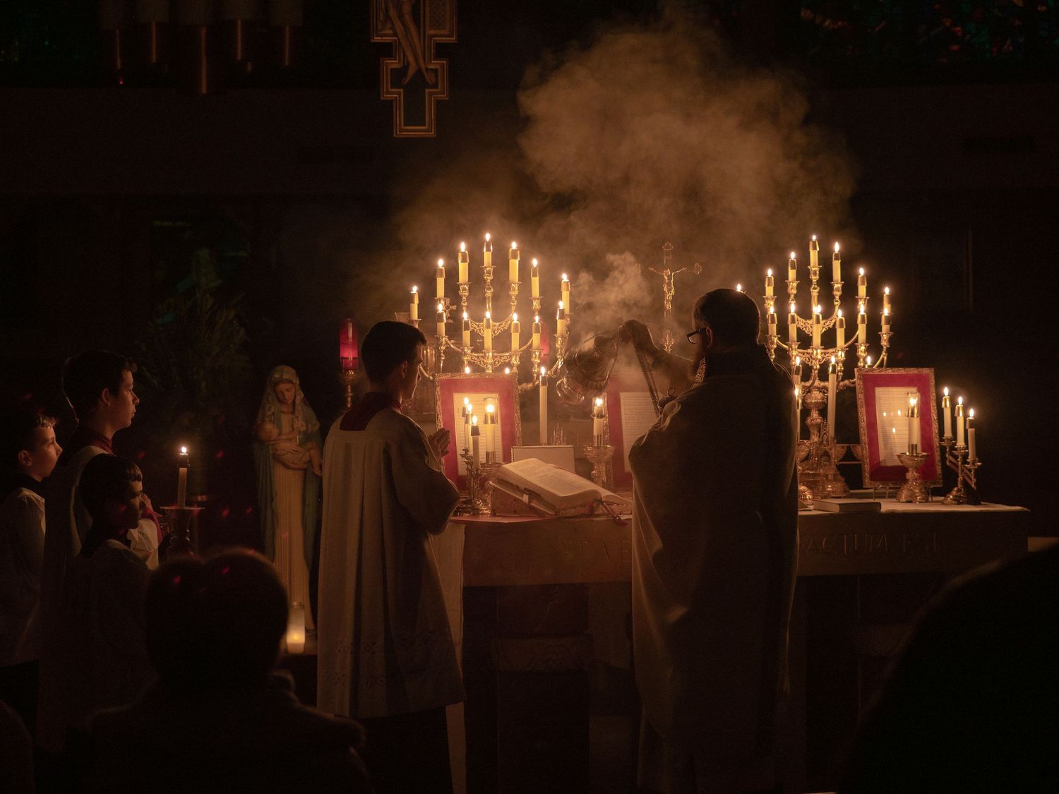Catholic altar ceremony with candles and incense smoke during traditional Latin Mass at night.