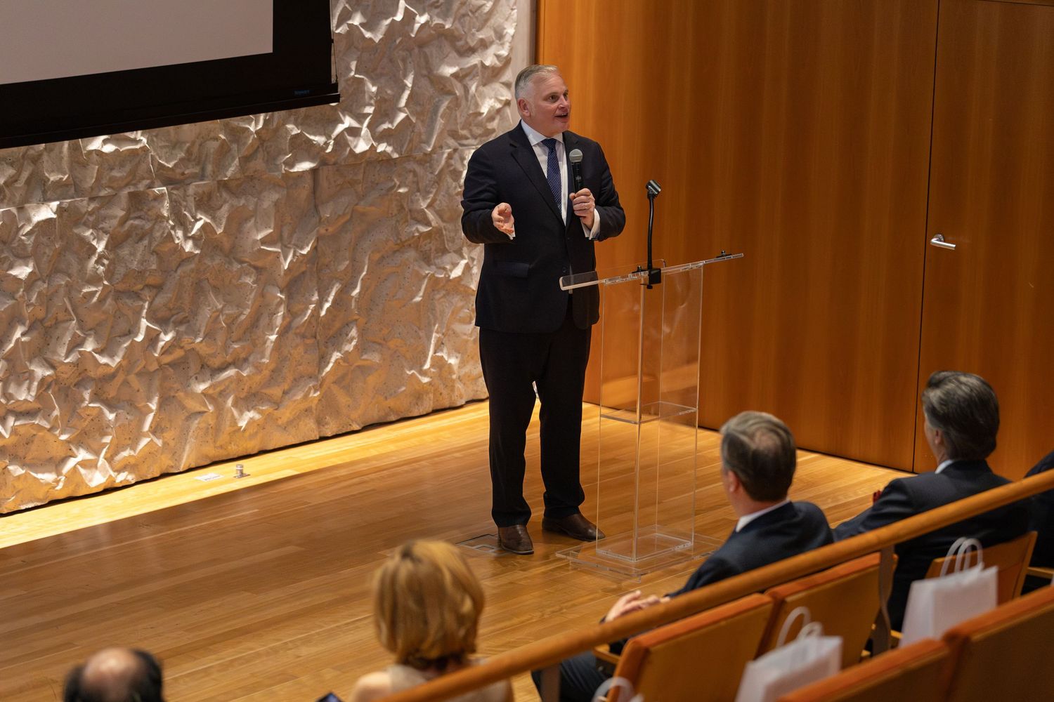 Business executive delivers keynote speech at corporate conference in modern auditorium with attentive audience.