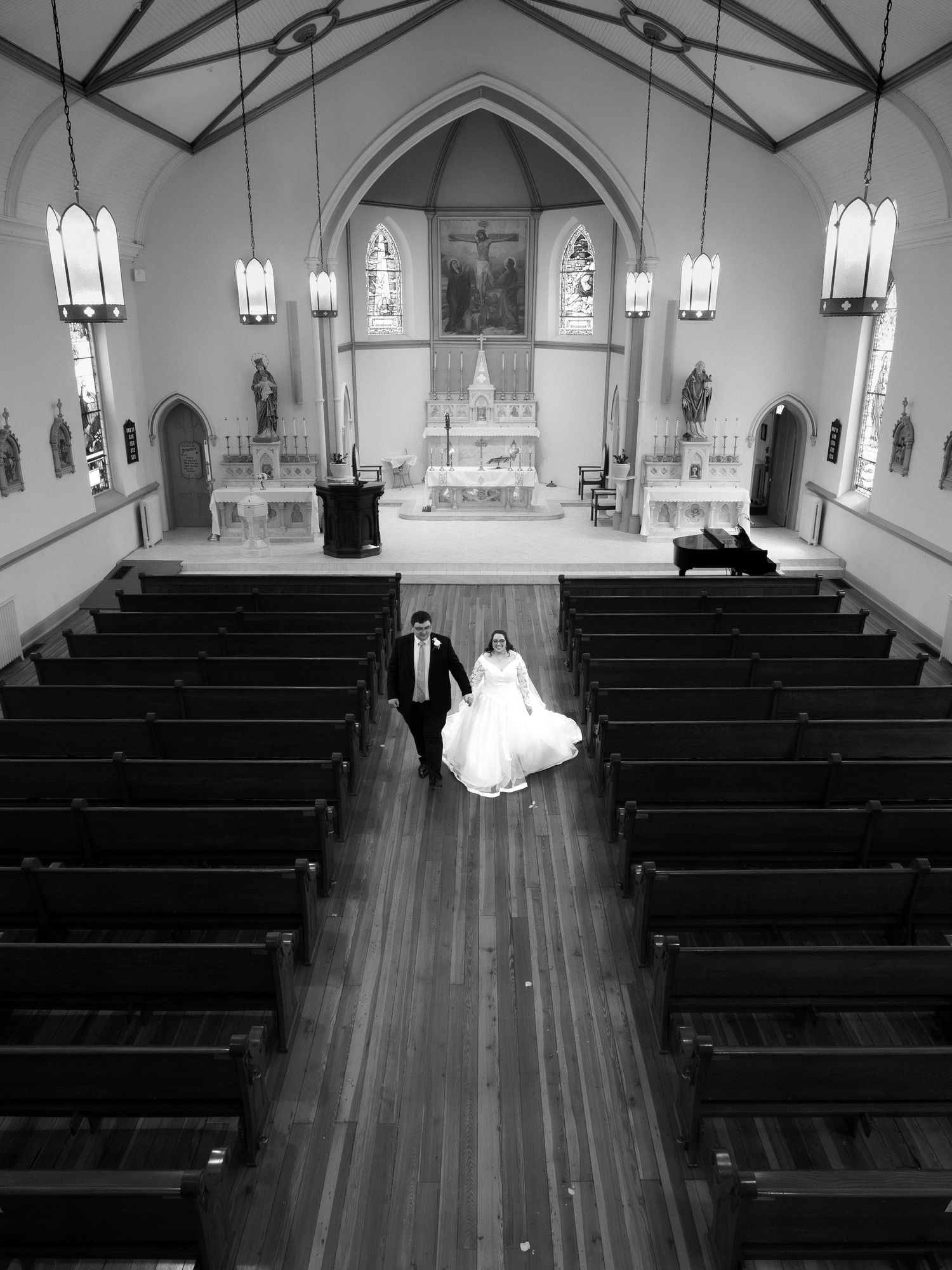 Black and white aerial view of newlywed couple walking down the aisle of a classic Catholic church after wedding.